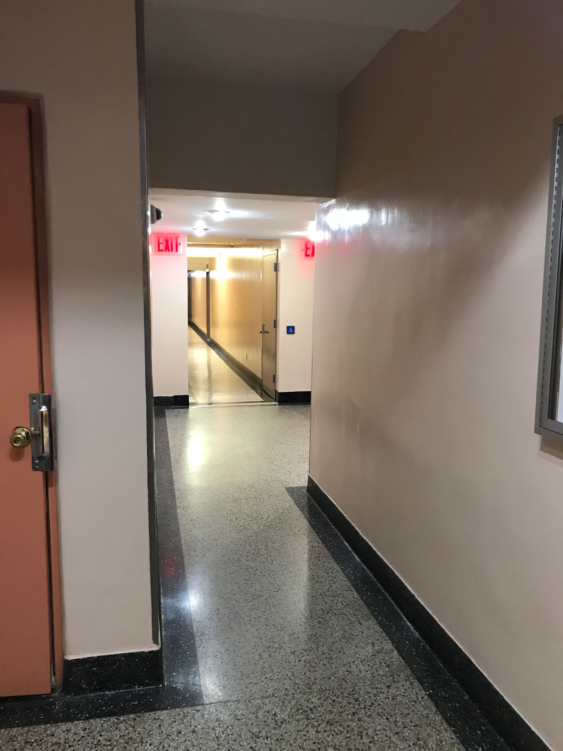 A long hallway with a red exit sign on the wall