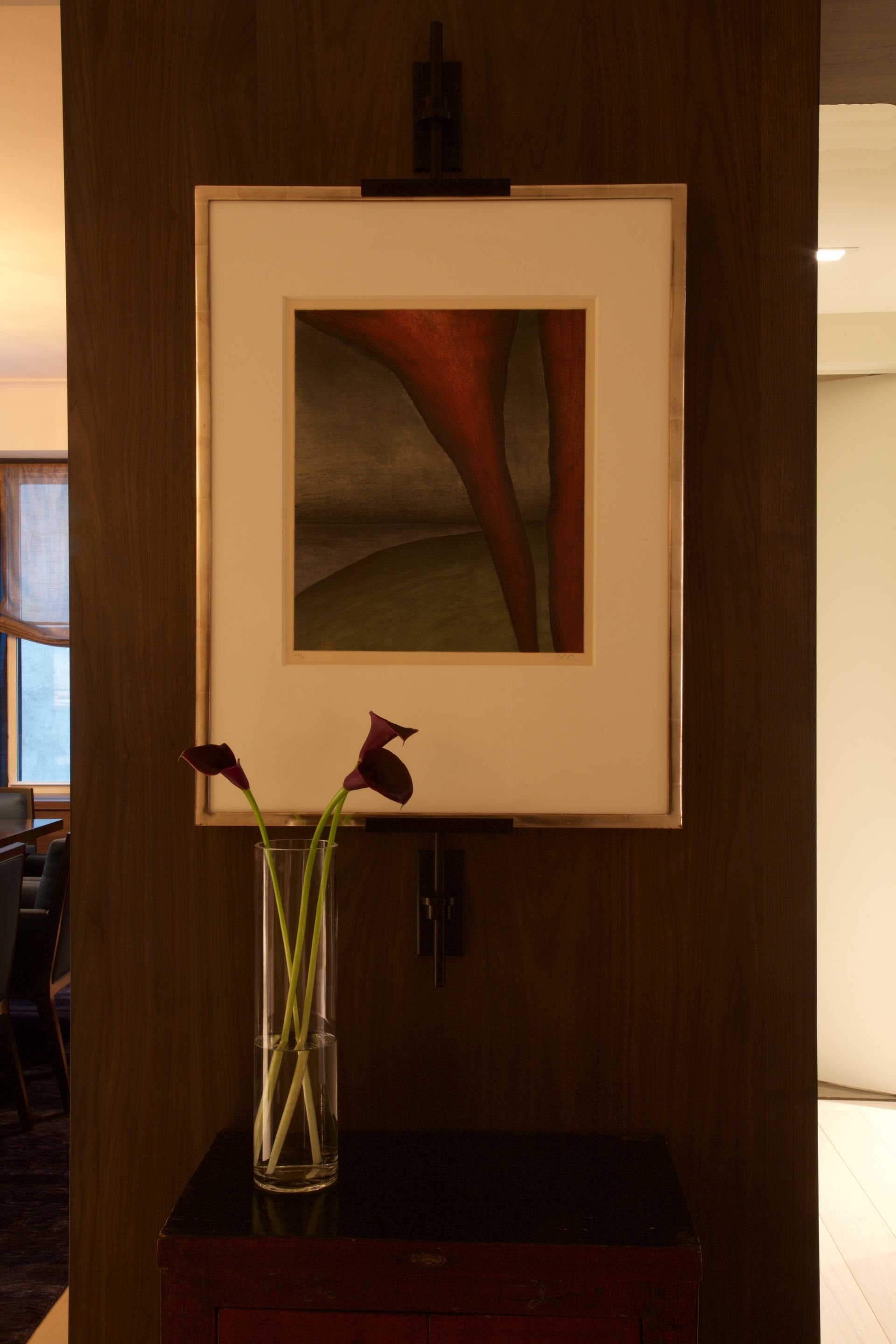 A framed picture hangs above a vase of flowers