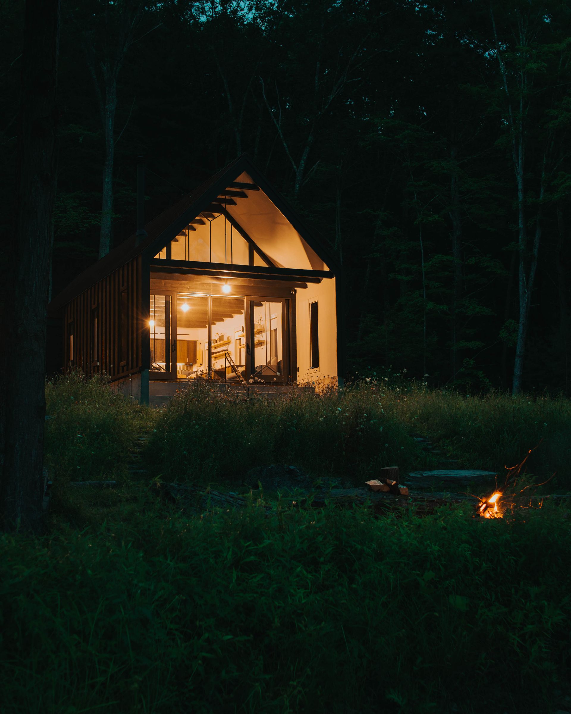 A small house is lit up at night in the middle of a forest.