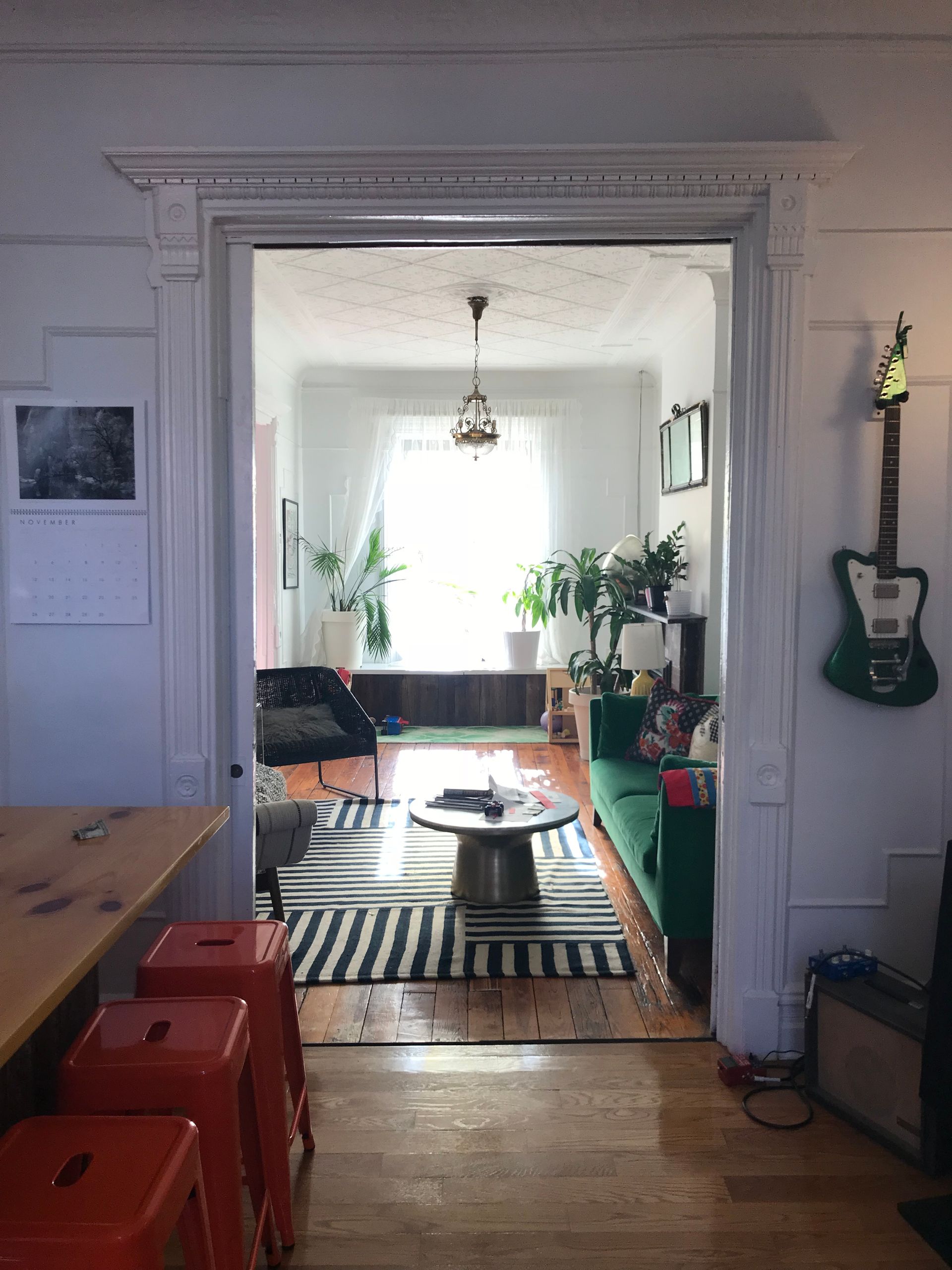 A living room with a green couch and a guitar hanging on the wall.