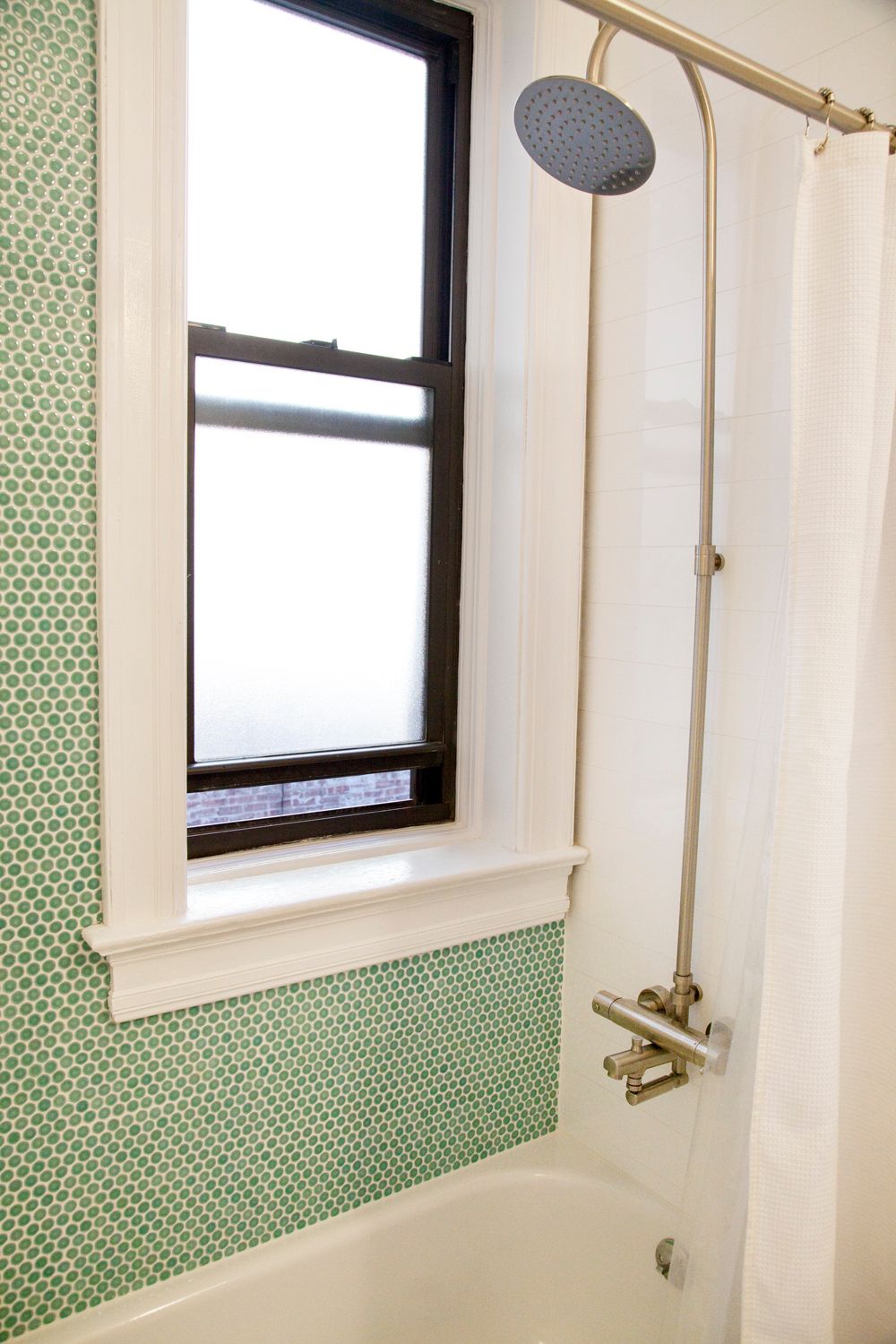 A shower head is hanging over a bathtub in a bathroom next to a window.