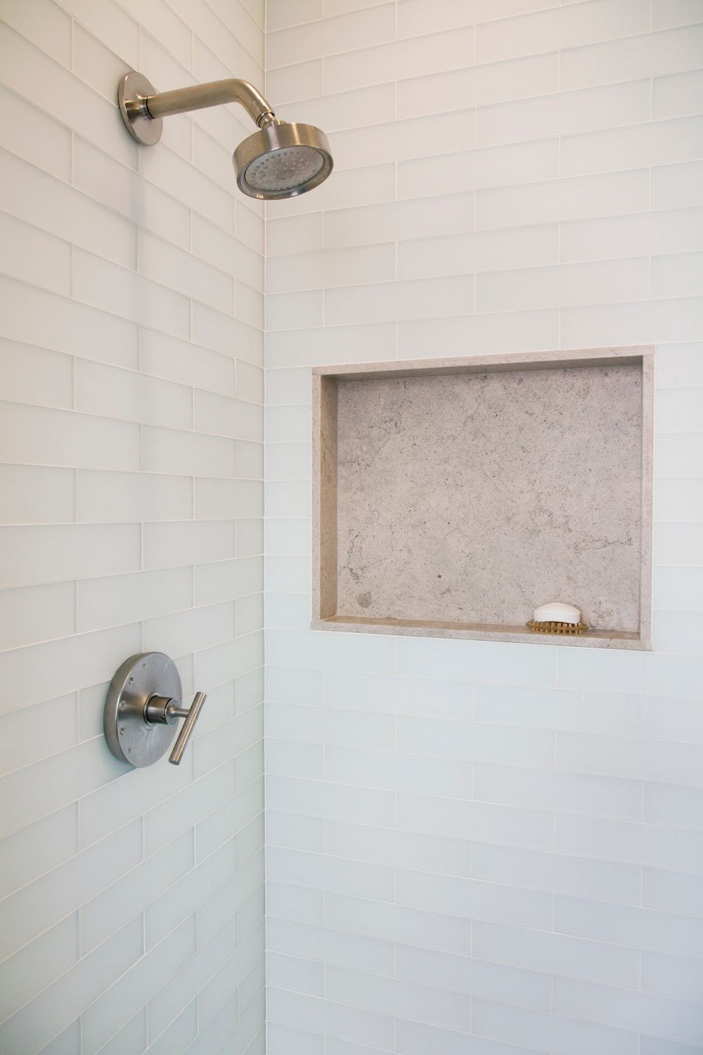 There is a shower head in the shower with a soap dish.