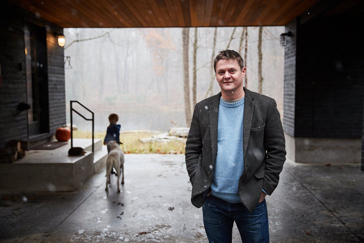 A man is standing in front of a house with his hands in his pockets.