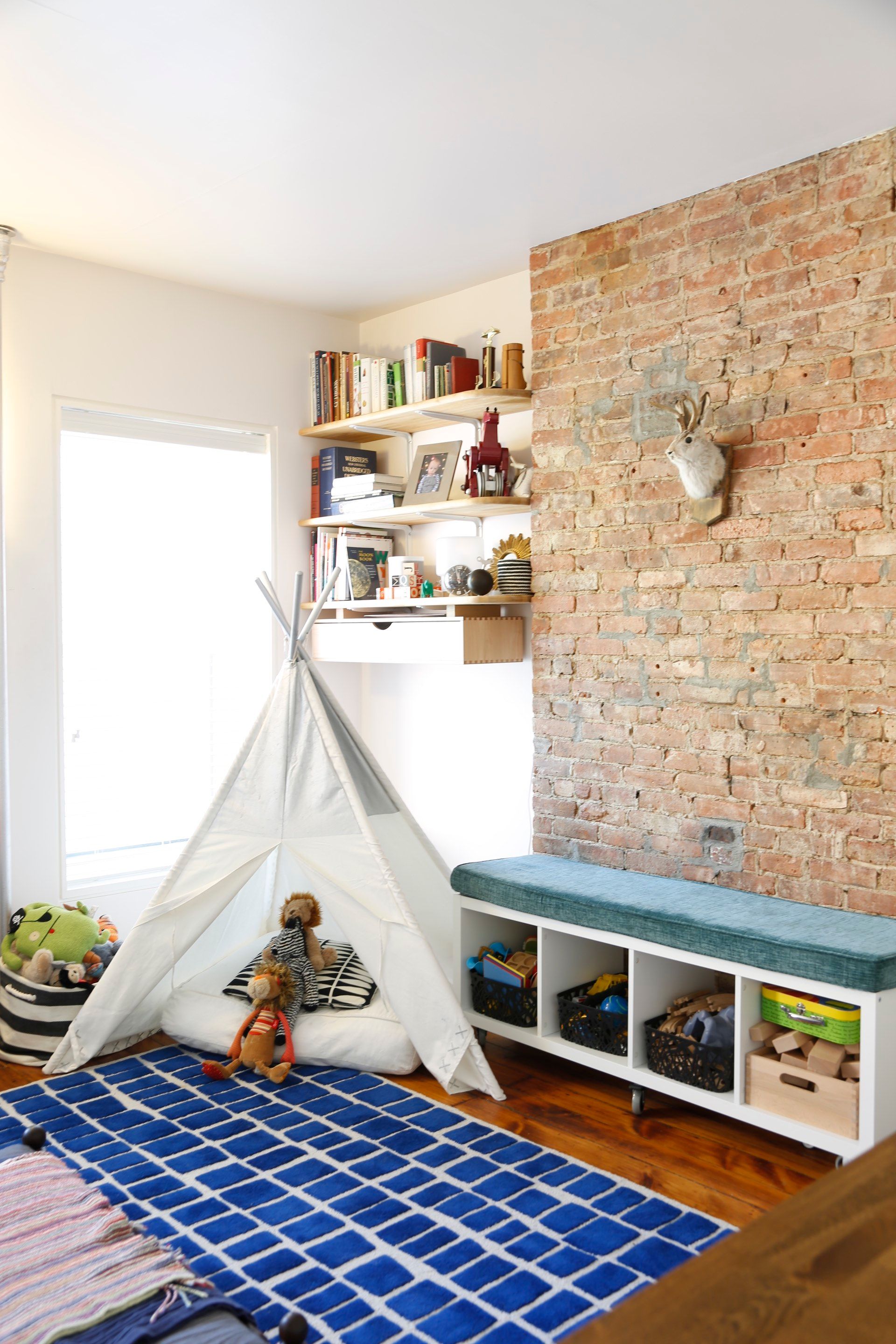 A child is sitting in a teepee in a room with a brick wall.