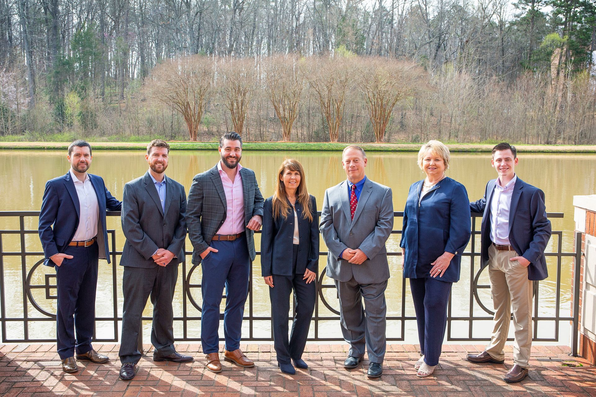 Group of seven professionals standing by a lake, all in business attire.