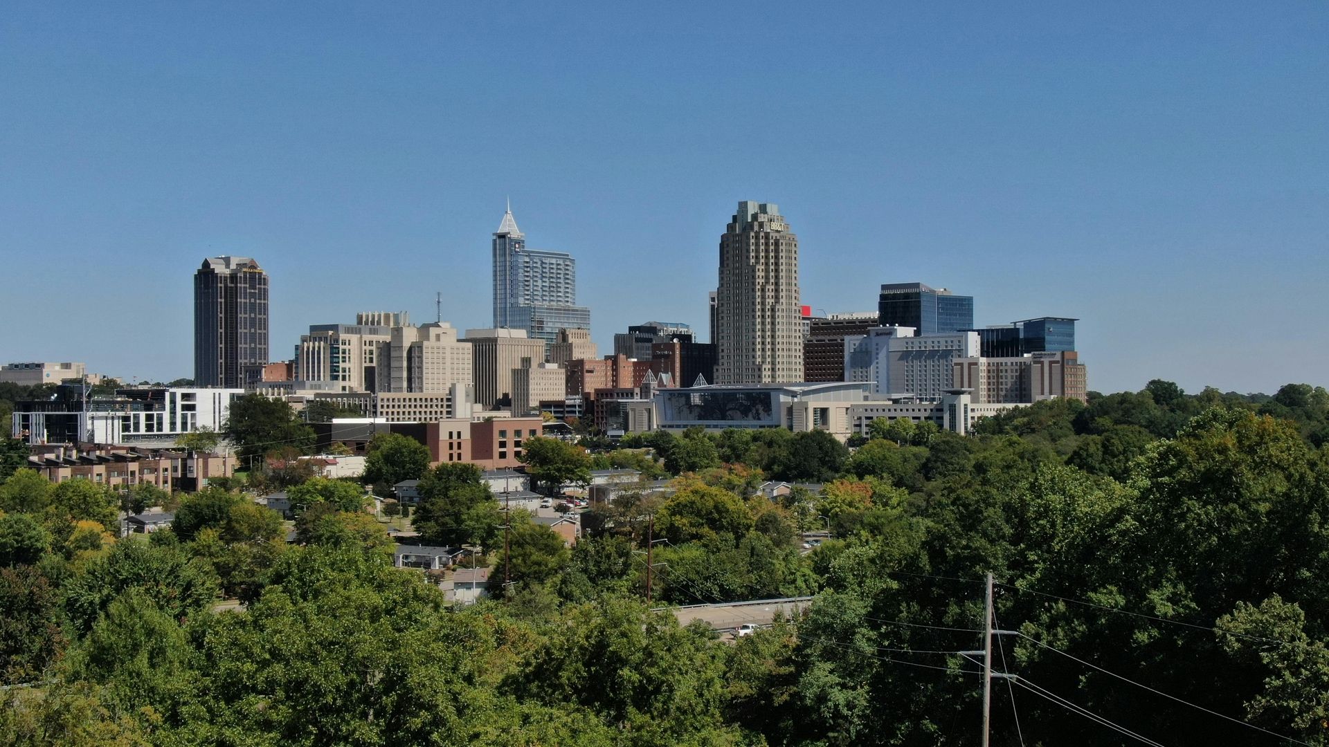 Charlotte, North Carolina skyline with skyscrapers and trees under a clear blue sky.