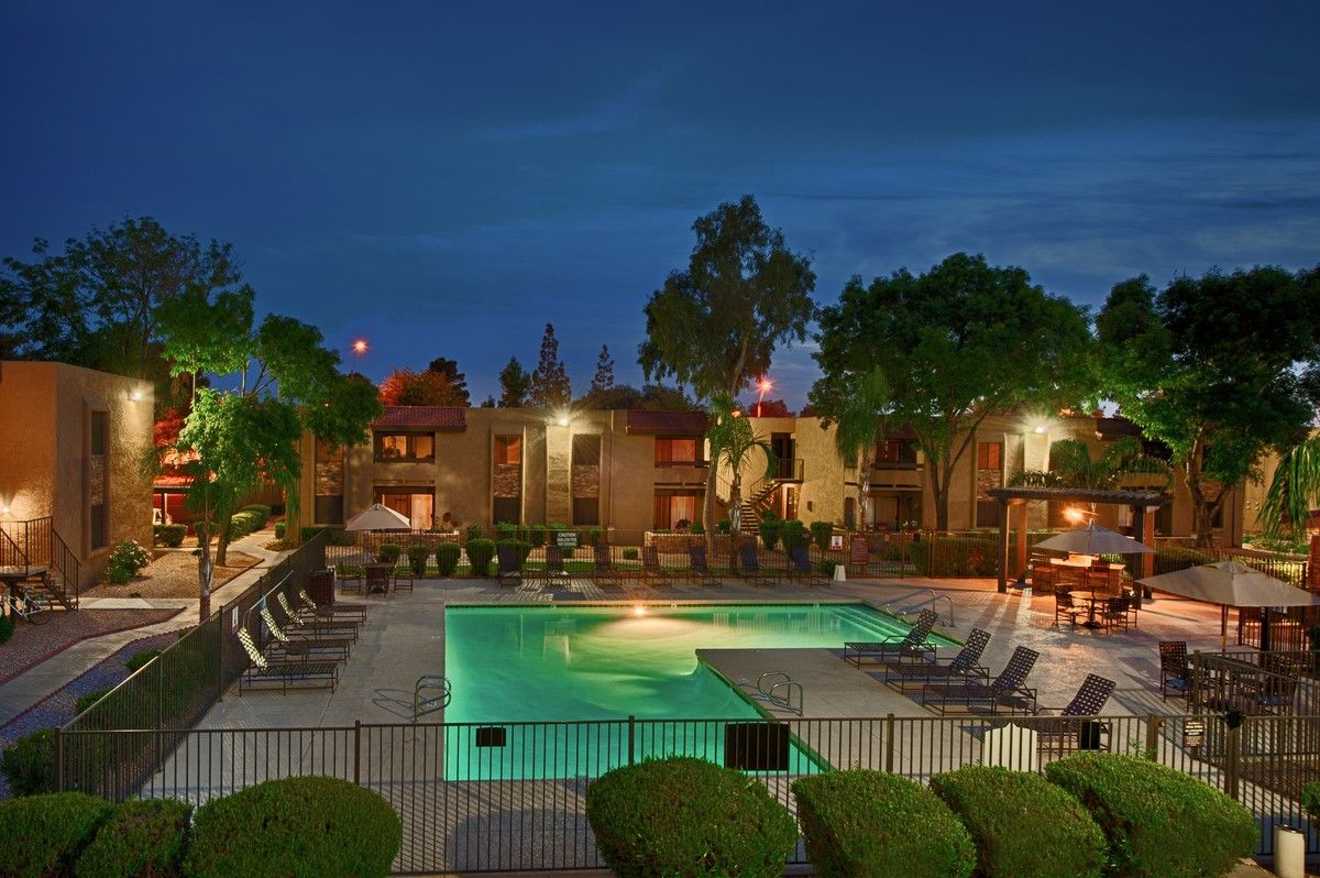 Outdoor resort pool at dusk with turquoise water, lounge chairs, and warm garden lighting