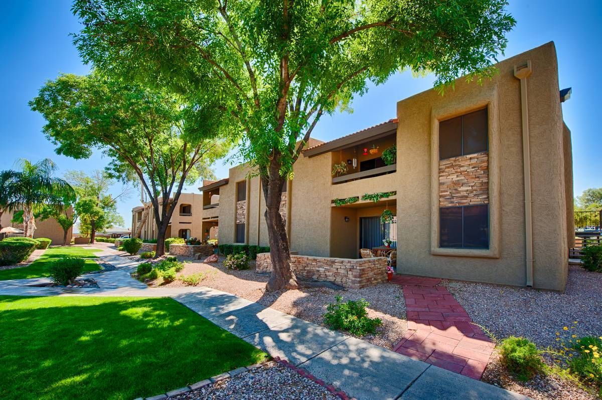 Apartment complex exterior with beige buildings, green lawn, trees, and blue sky