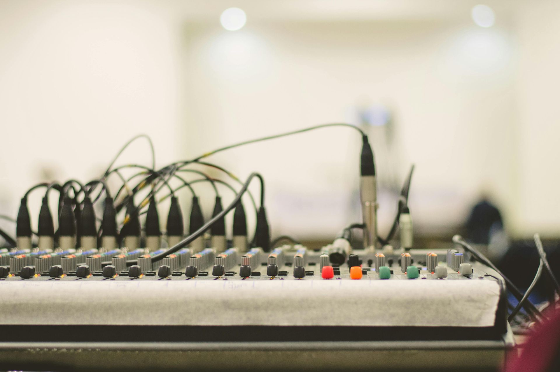A professional audio mixing console with multiple cables plugged into its top panel in a brightly lit studio setting.