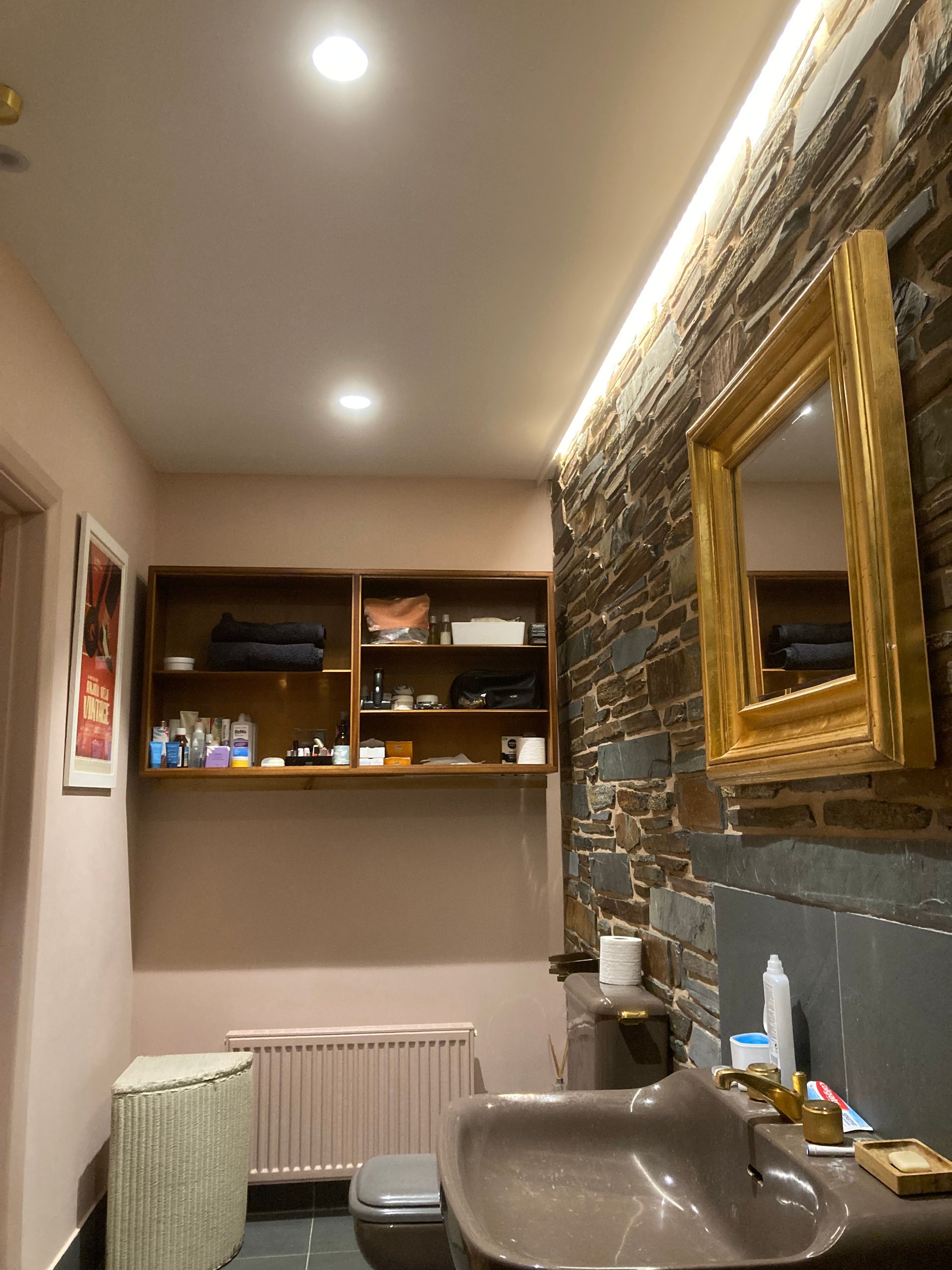 A bathroom with a sink , toilet , mirror and shelves.