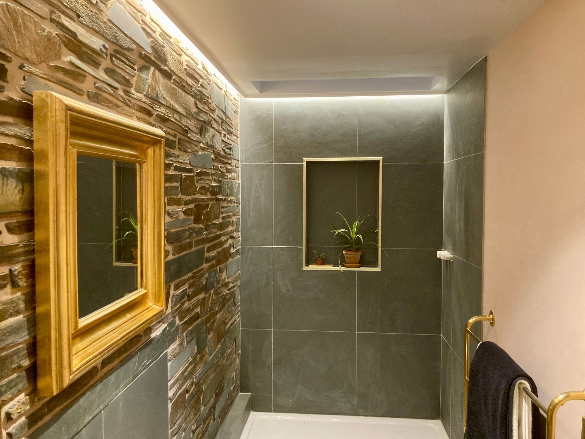 A bathroom with a stone wall and a gold mirror