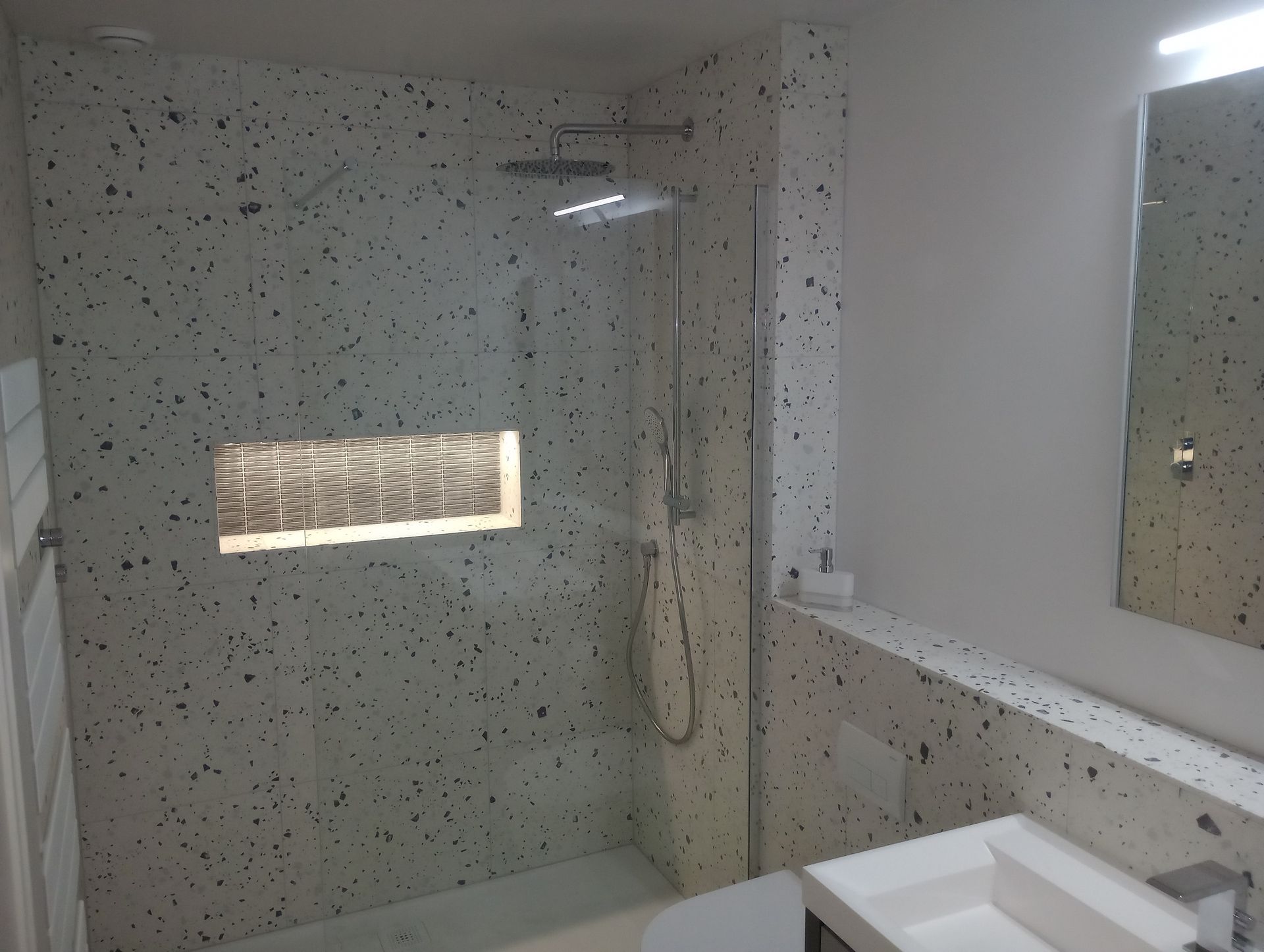 A bathroom with a walk in shower and a sink with lighting