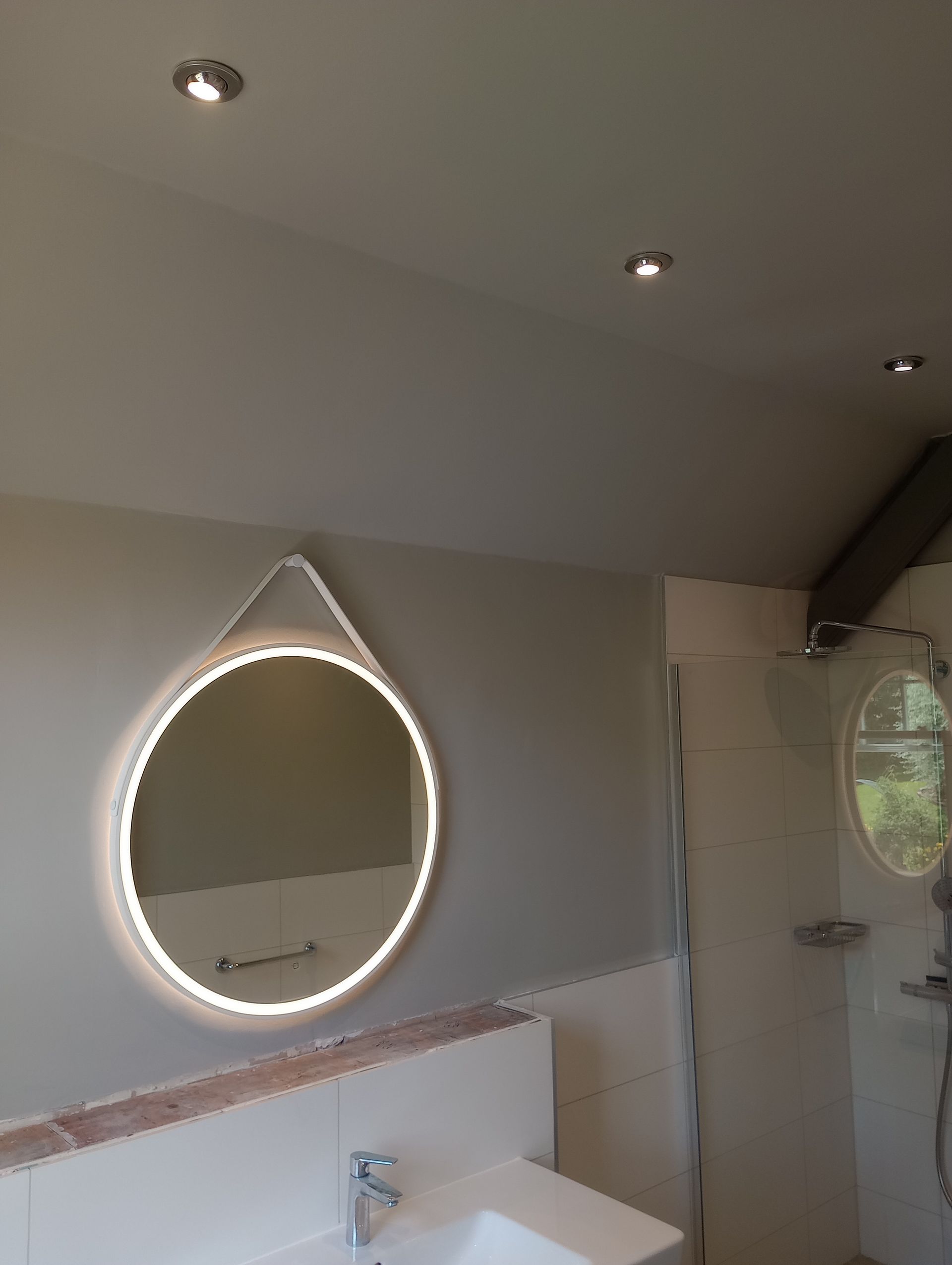 A bathroom with a sink and a round mirror on the wall with lighting.