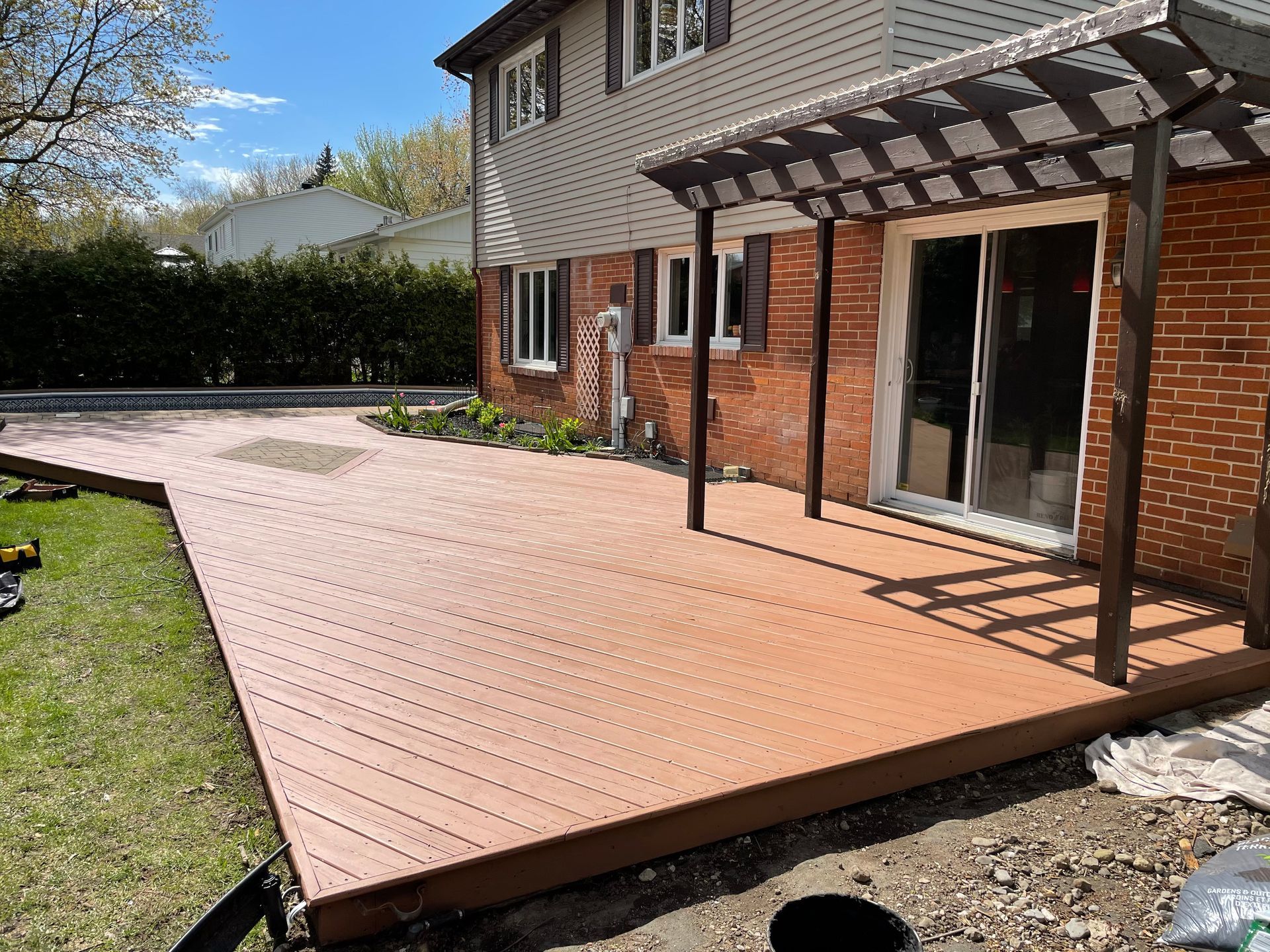 Une terrasse en bois avec une pergola et une maison en briques en arrière-plan.