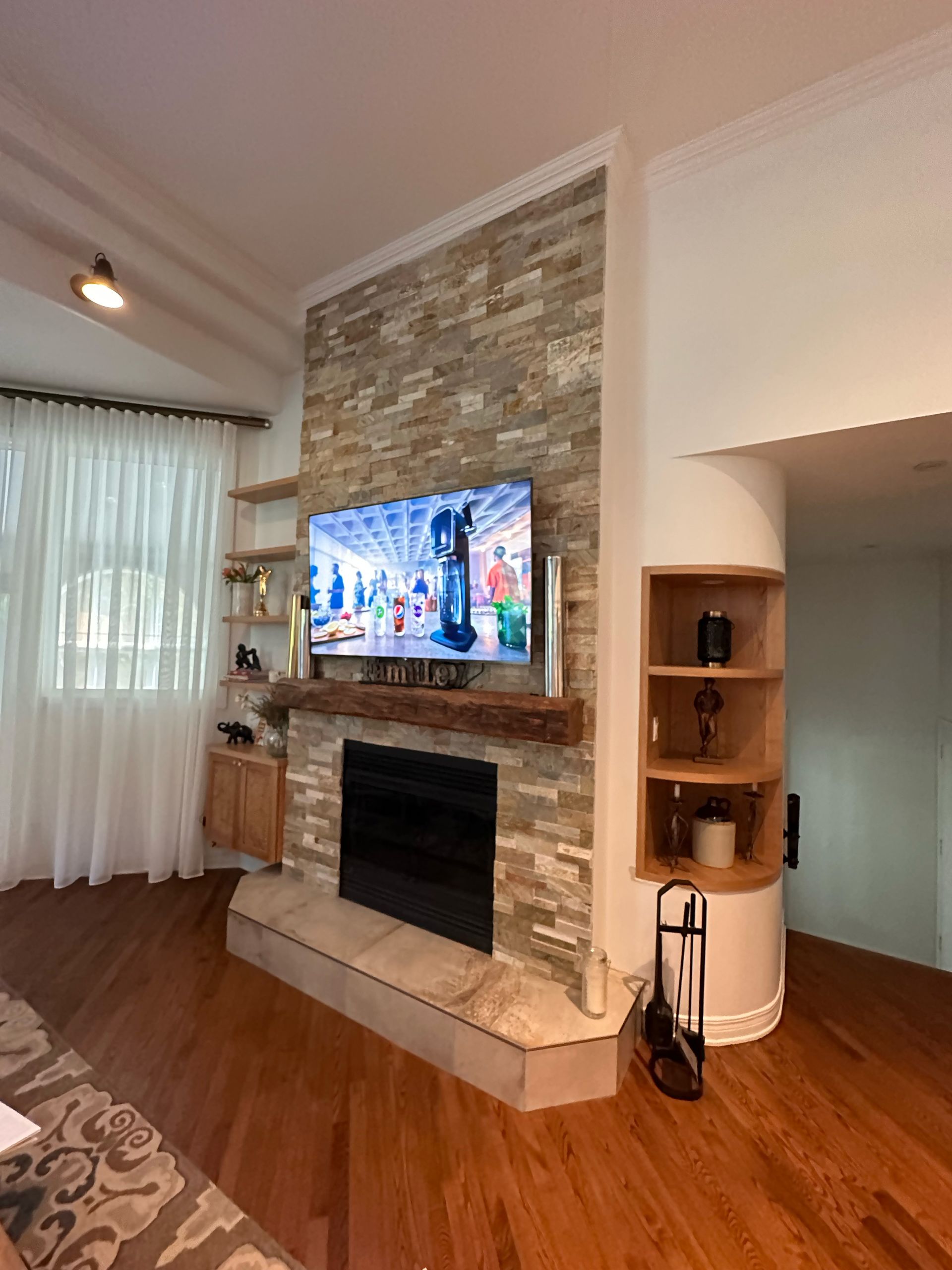 Salon avec cheminée en pierre, télévision, rangements intégrés et parquet.