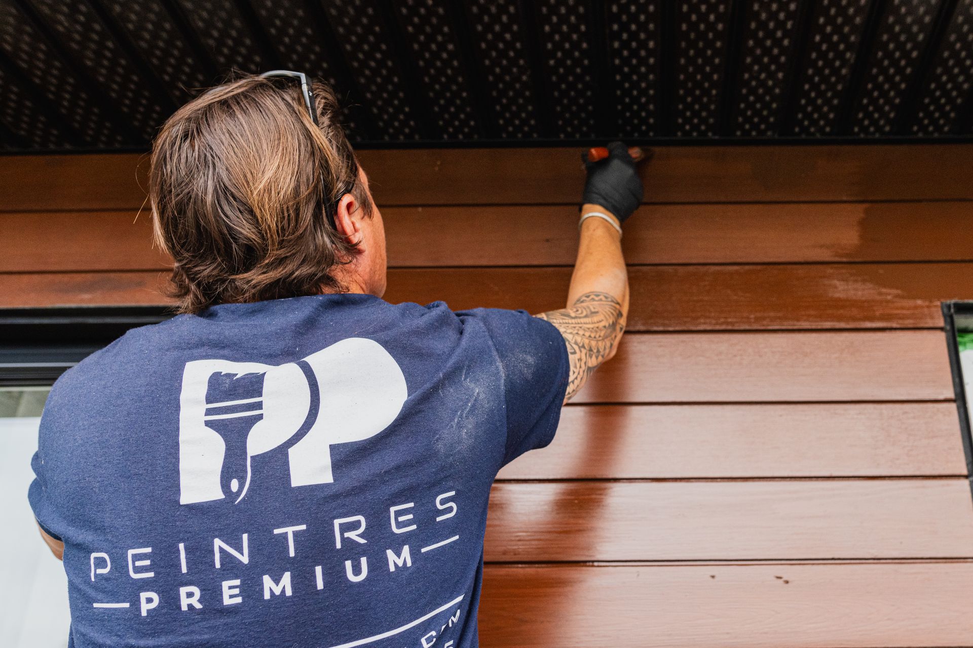 Un homme en chemise bleue peint un mur en bois.