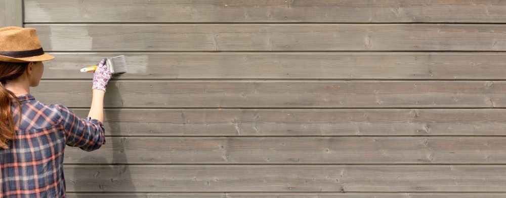 Une femme peint un mur en bois avec un pinceau.