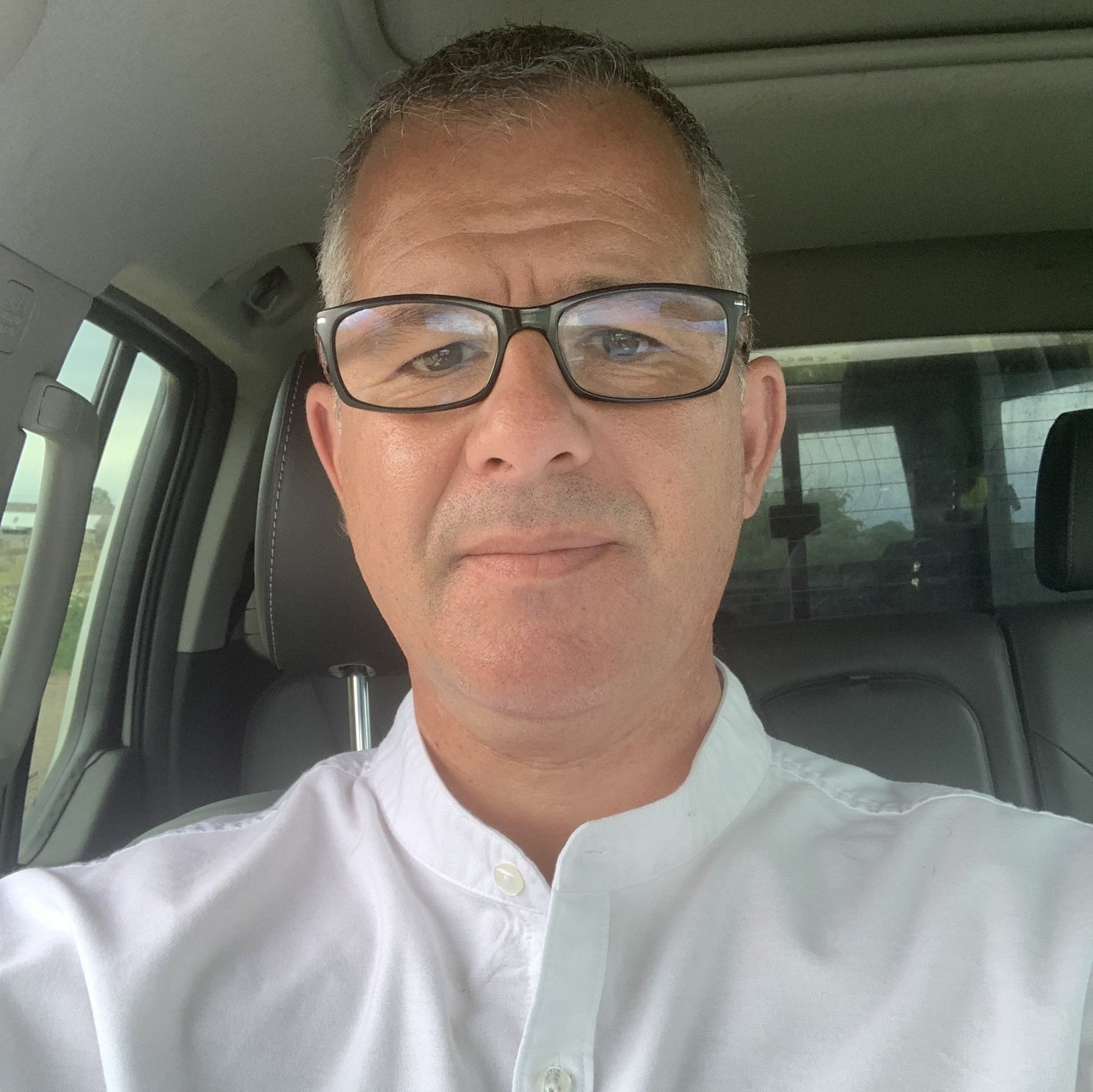 A man wearing glasses and a white shirt is sitting in a car.