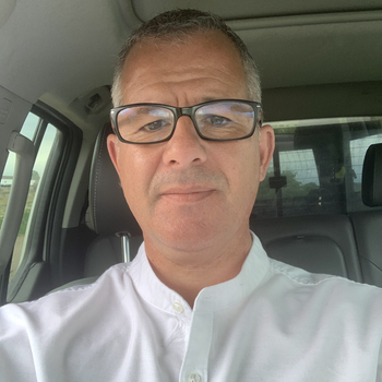 A man wearing glasses and a white shirt is sitting in a car.