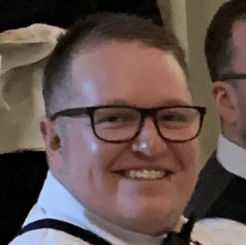 A man wearing glasses and a bow tie is smiling for the camera.