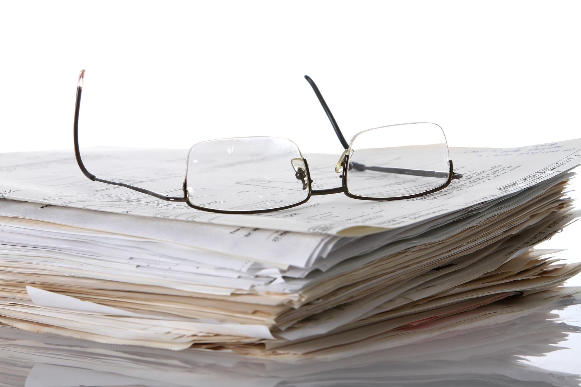 A pair of glasses sitting on top of a pile of papers