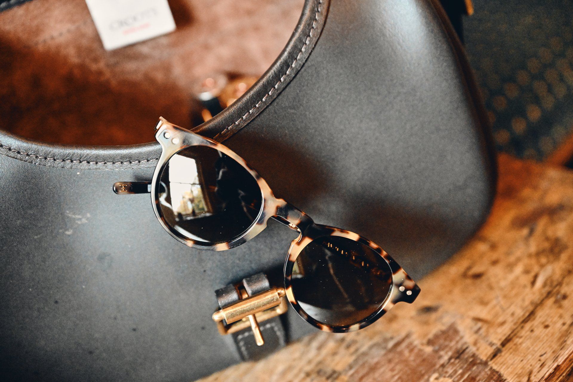 Sunglasses with tortoiseshell frames rest on a dark gray handbag.