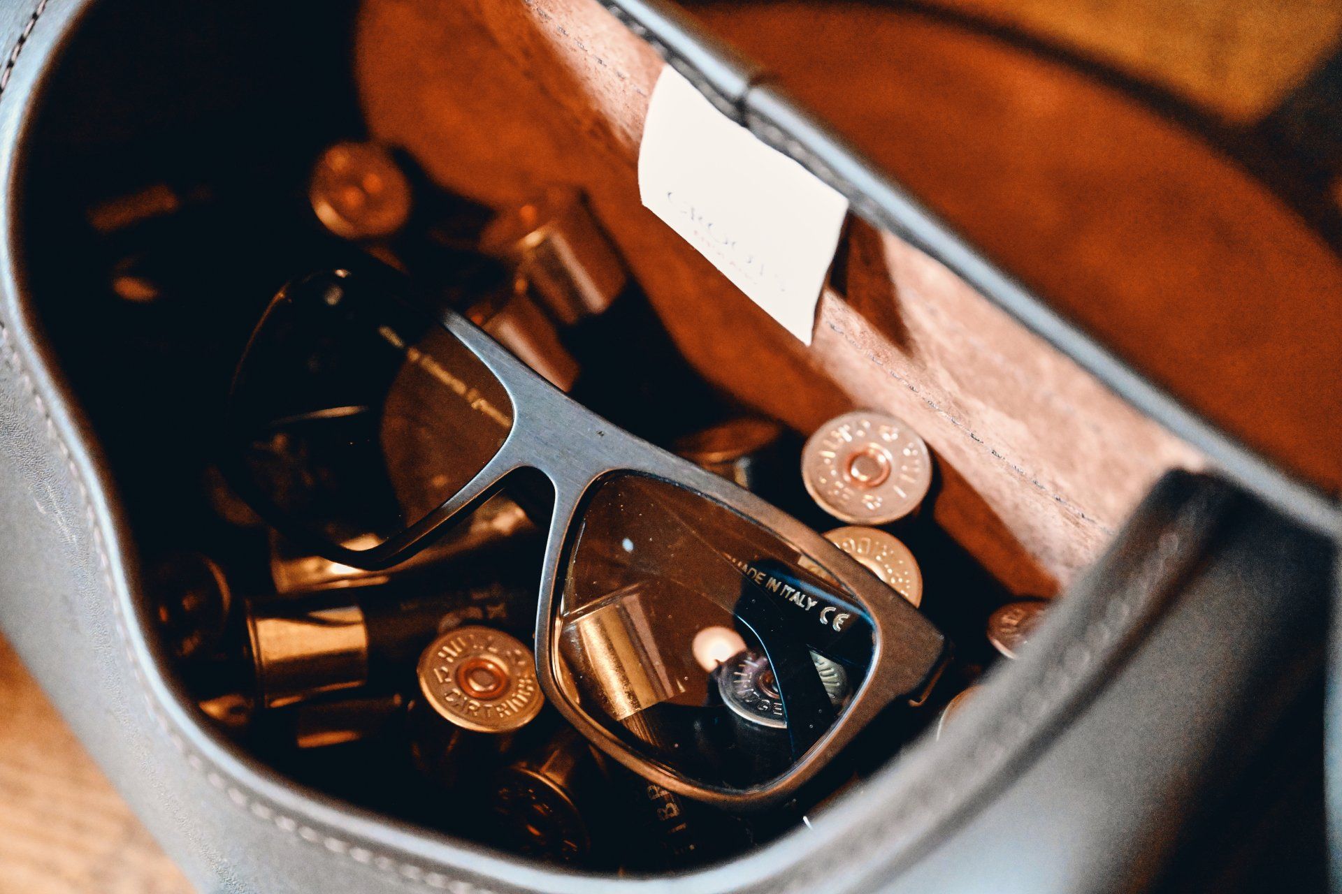 Sunglasses inside a dark bag filled with scattered shotgun shells.