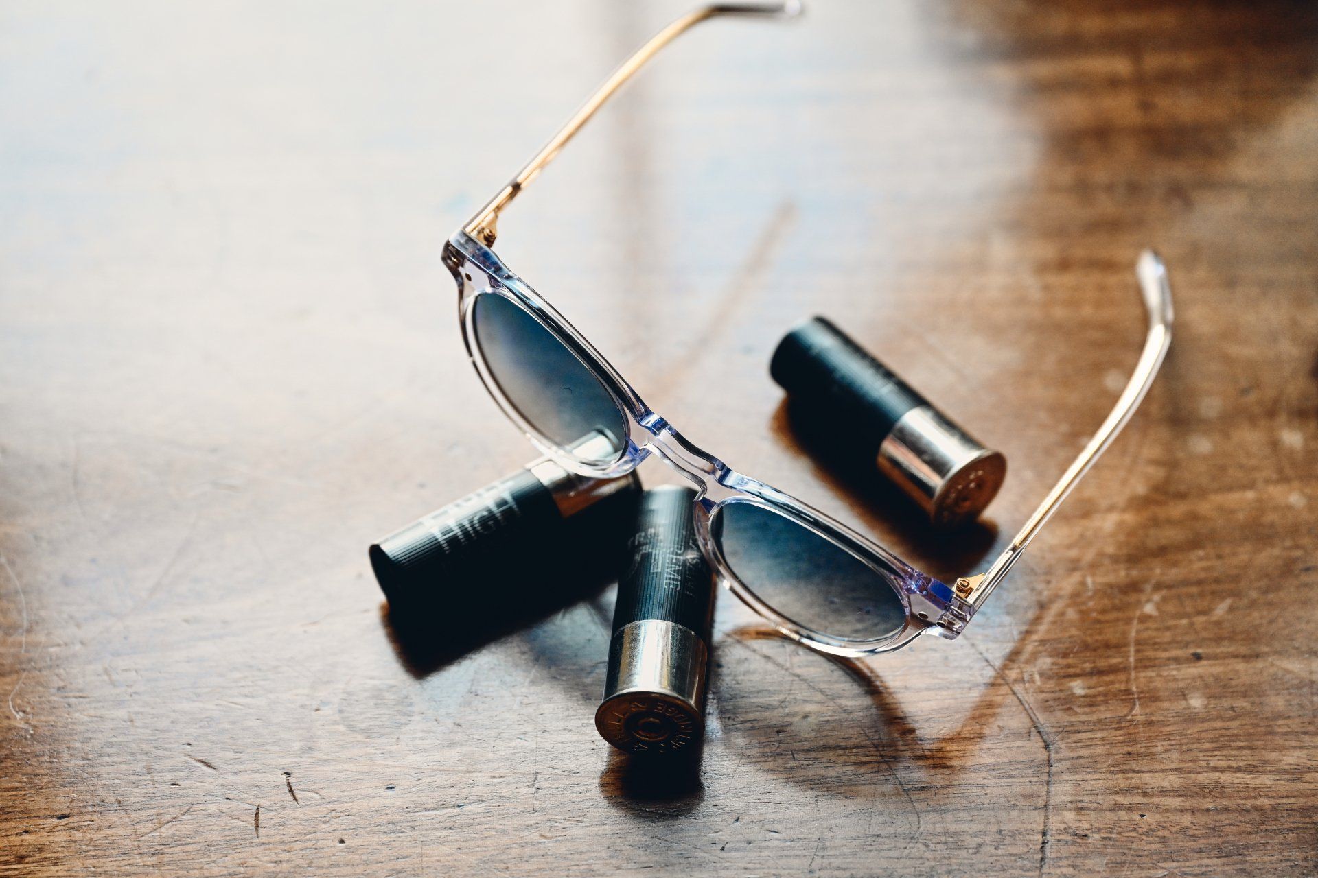 Sunglasses and three lipsticks on a wooden surface.