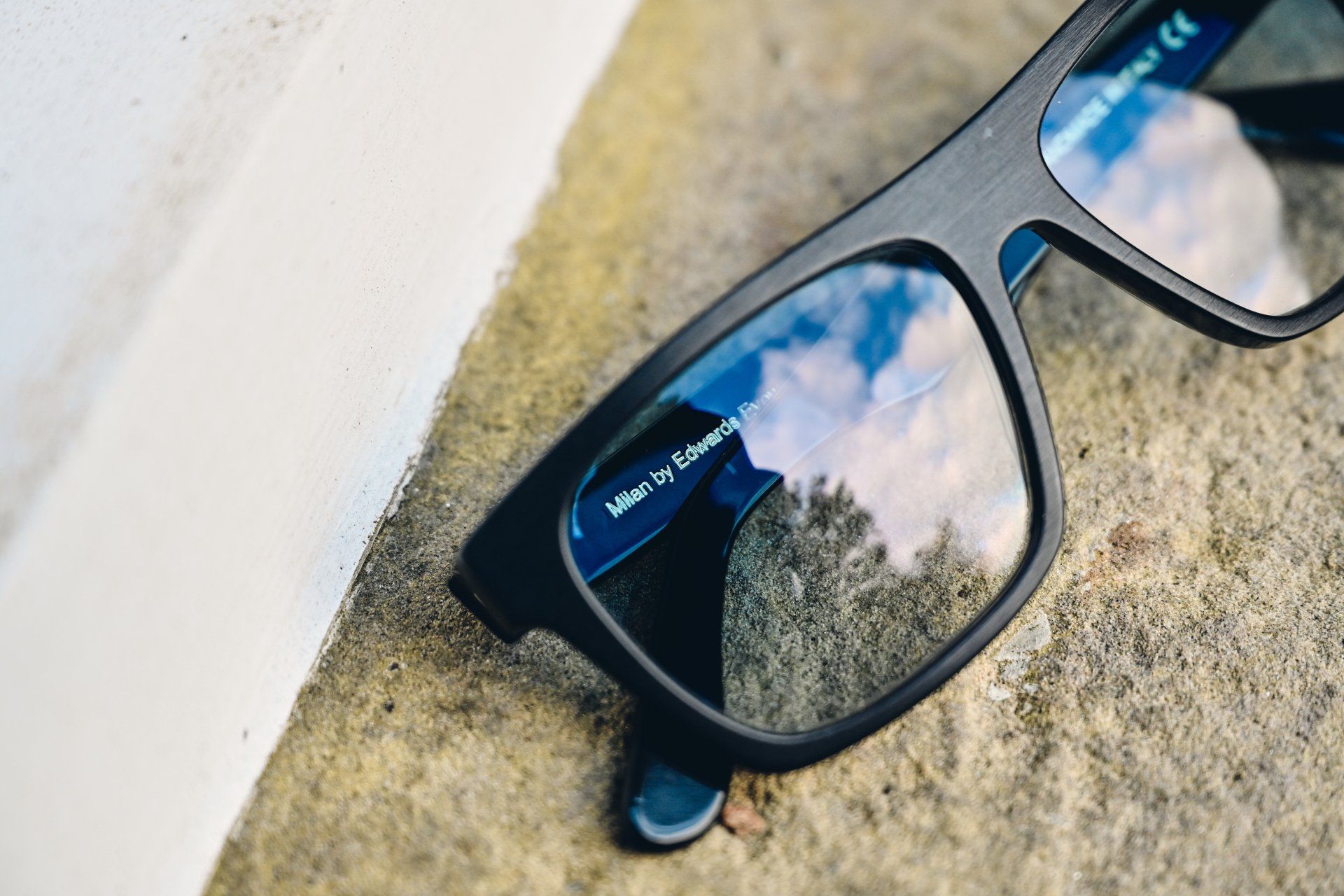 Black-framed eyeglasses on a textured stone surface, reflecting the sky.