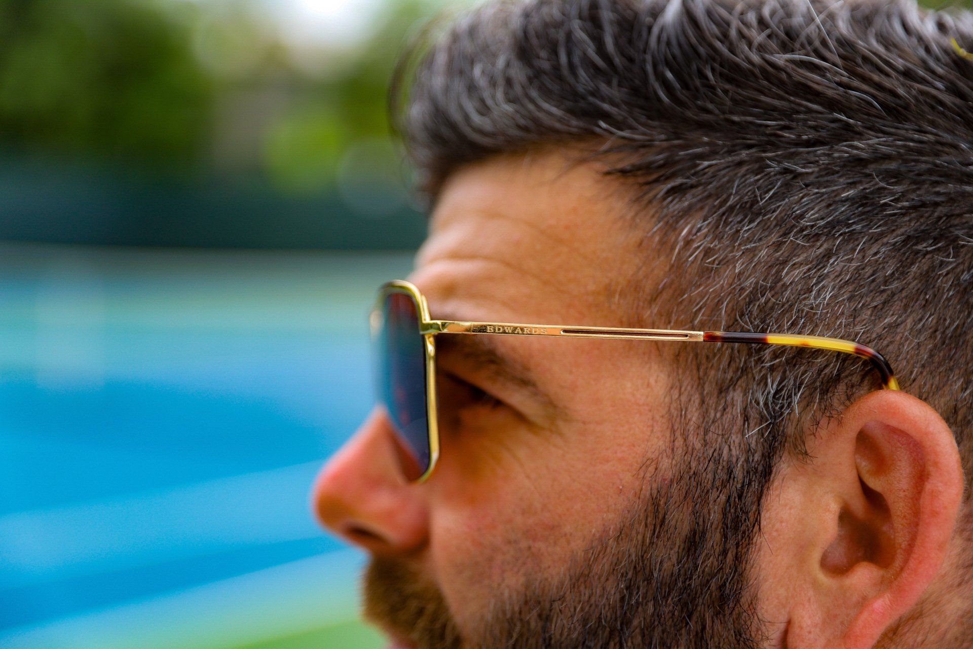 Man with sunglasses, short gray hair, and beard, looking left. Blue background.