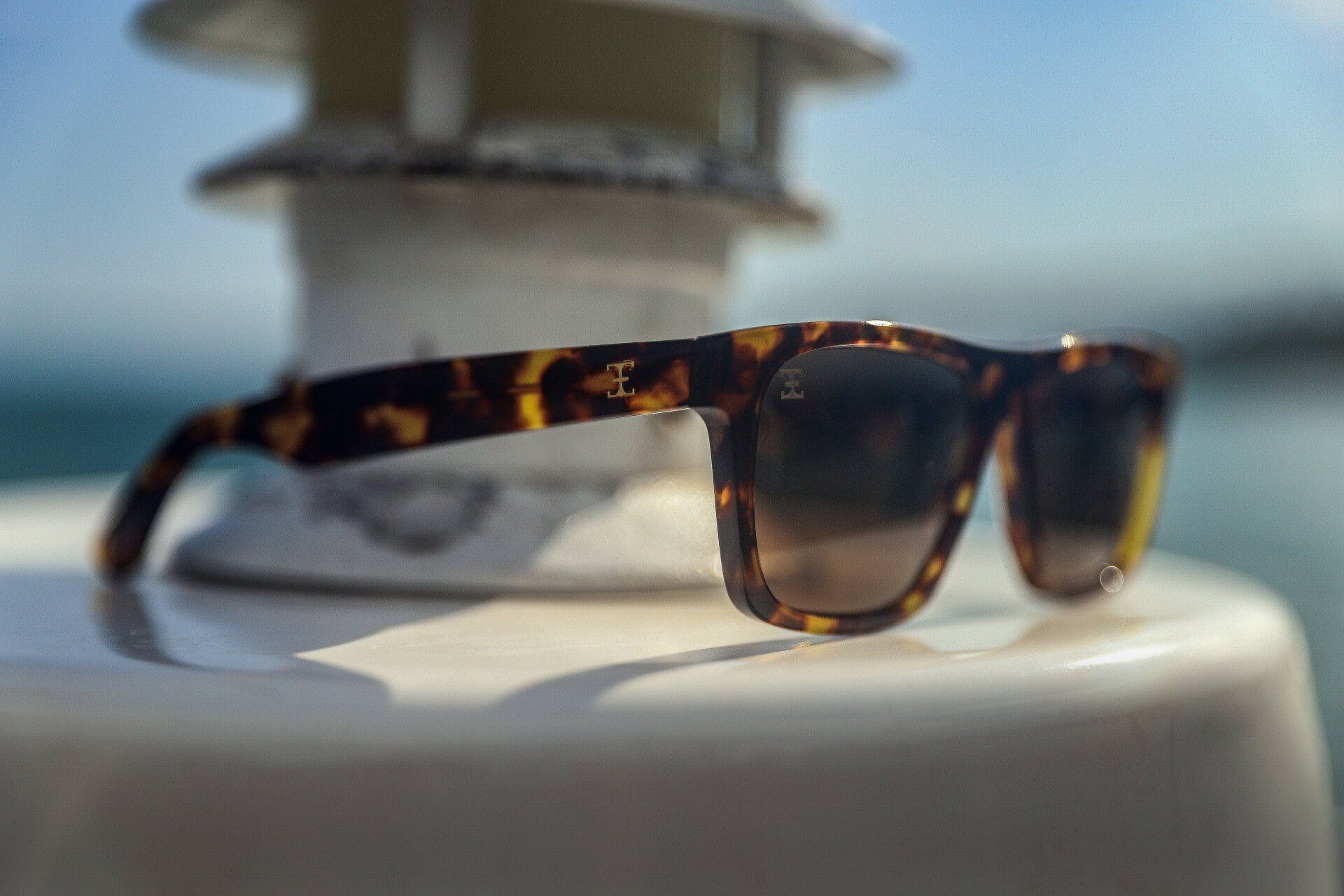 Sunglasses with tortoise shell frames rest on a white lighthouse, ocean in the background.