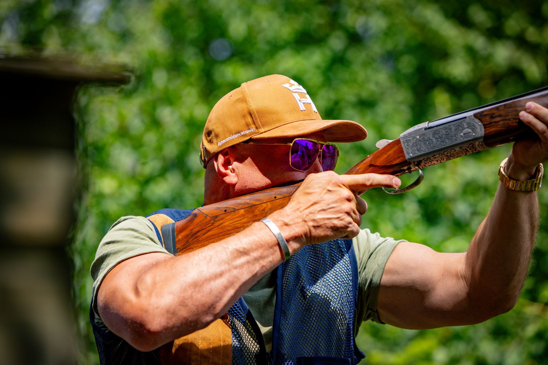 Man aiming a shotgun; outdoors, wearing a cap and sunglasses, ready to shoot.