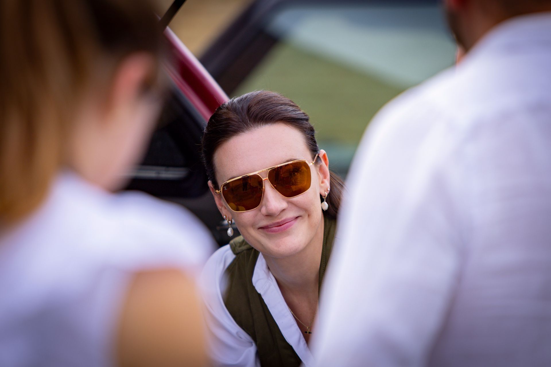 Woman in sunglasses smiles while speaking to two people.