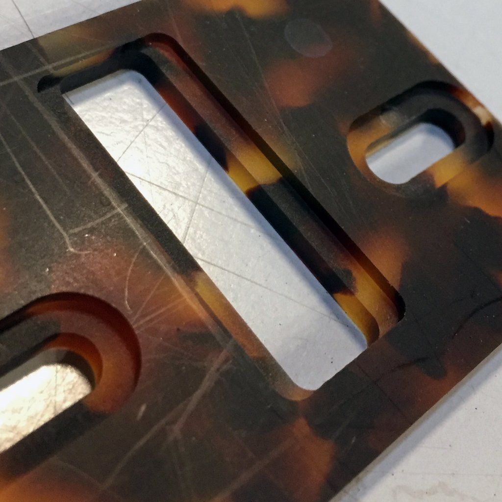 Tortoiseshell-patterned plastic piece with rectangular and circular cutouts, scratches on surface.