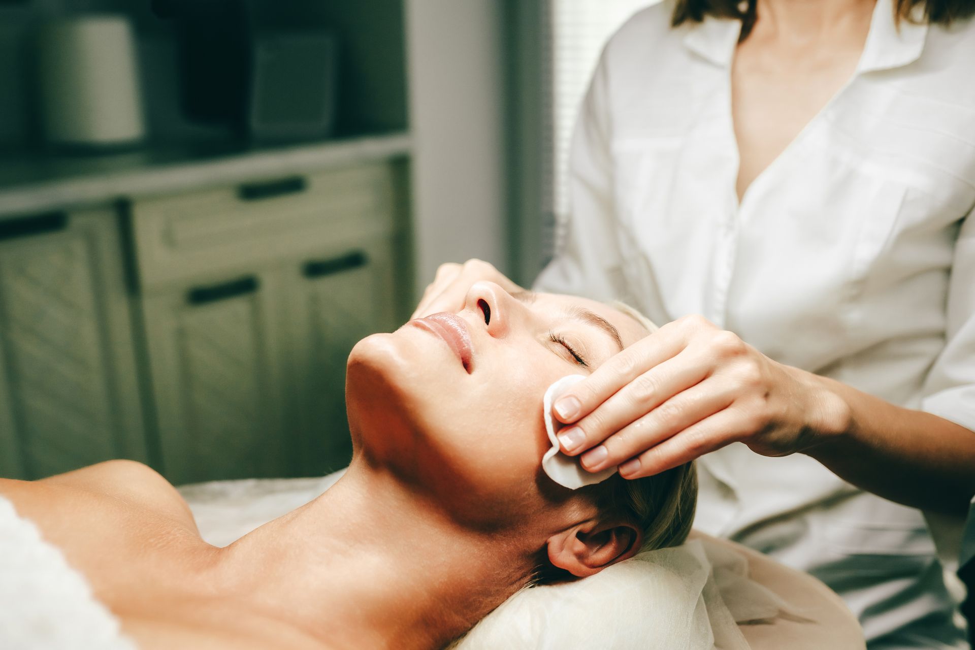 Donna che riceve un trattamento viso; estetista applica il prodotto con dischetti di cotone.