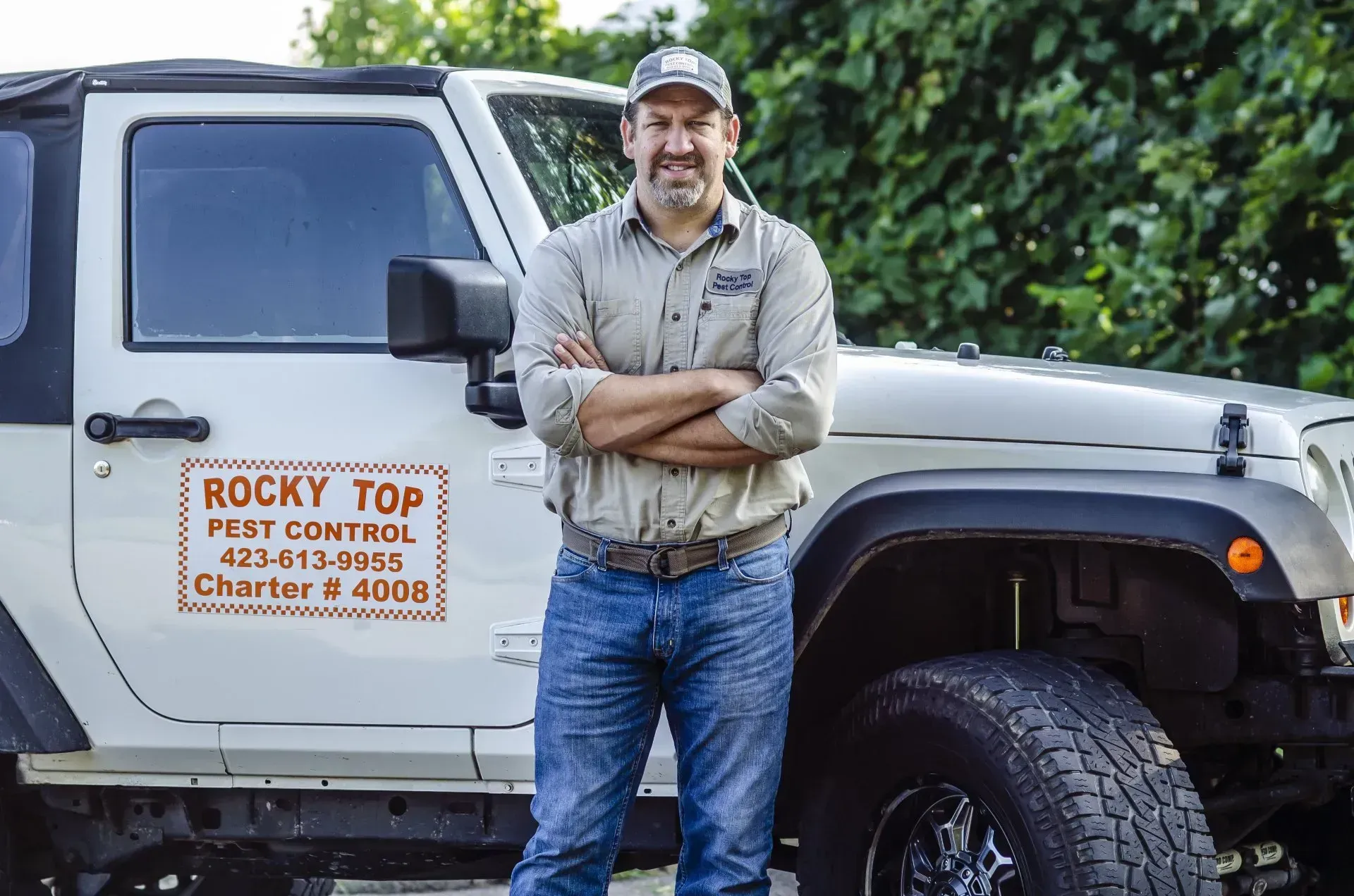 Man with crossed arms stands by a white Jeep; logo for