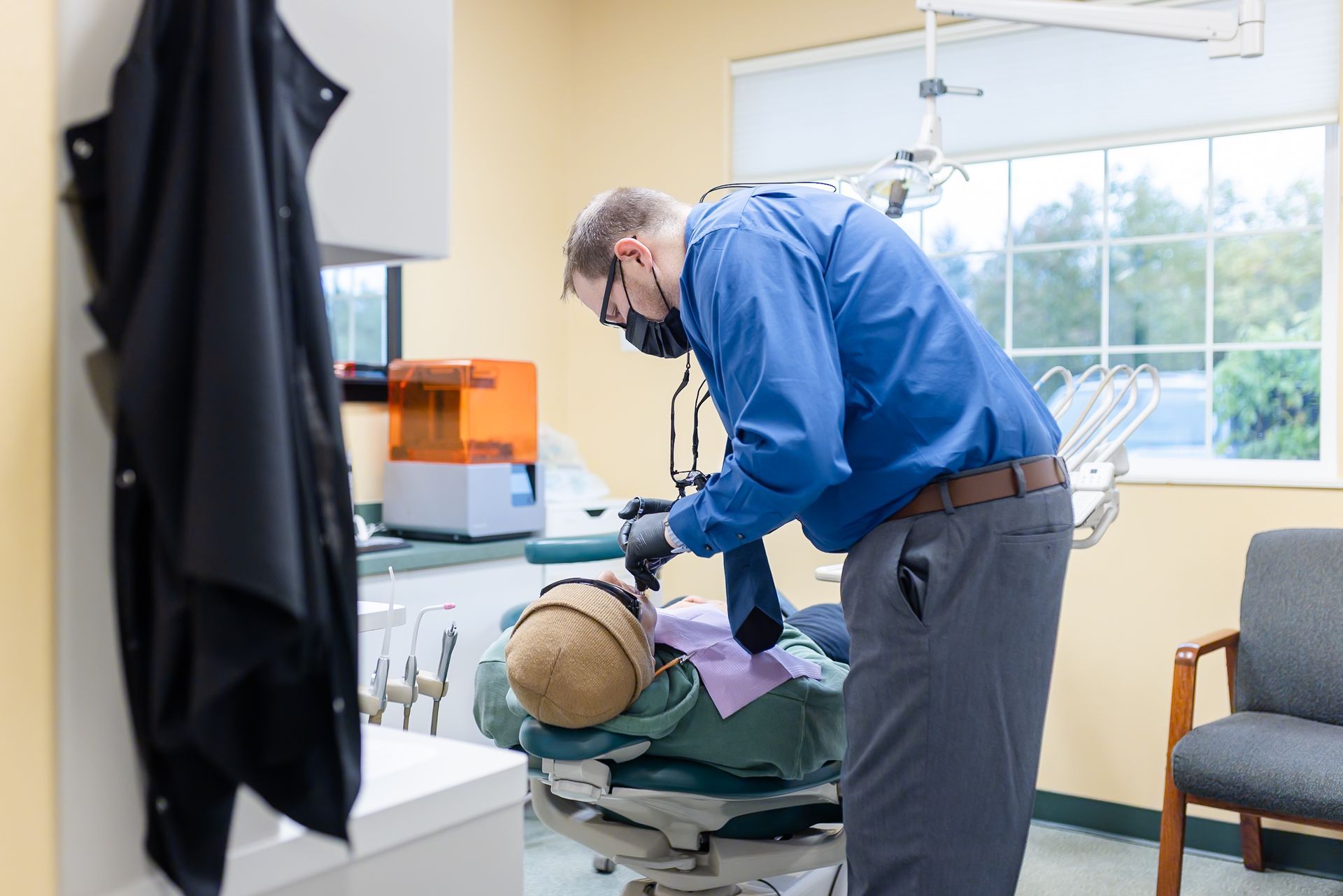 Dentist in blue scrubs gives high five to child patient wearing purple bib and sunglasses. Dental office setting.