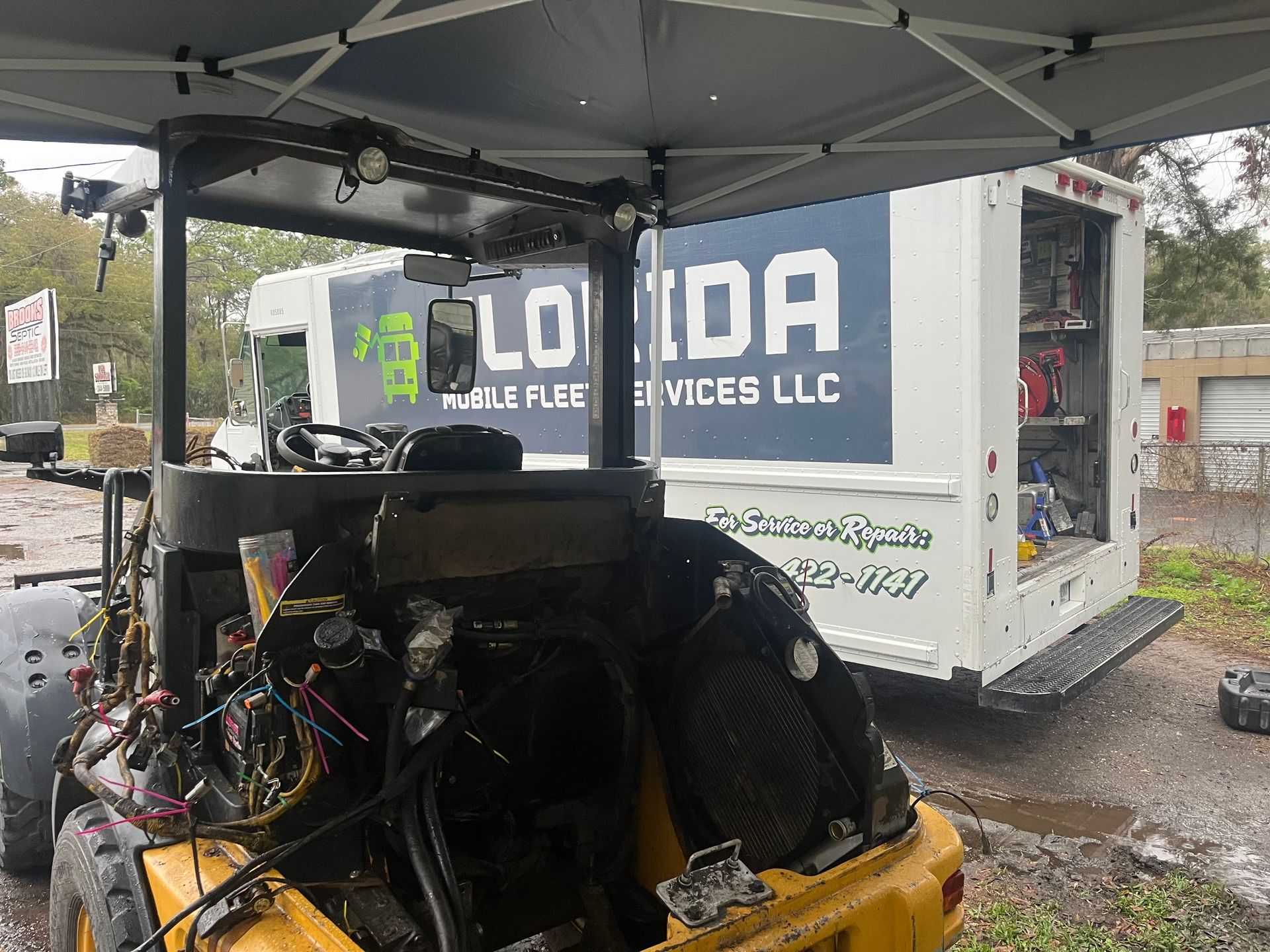 A forklift is sitting under a tent next to a truck that says florida services llc.