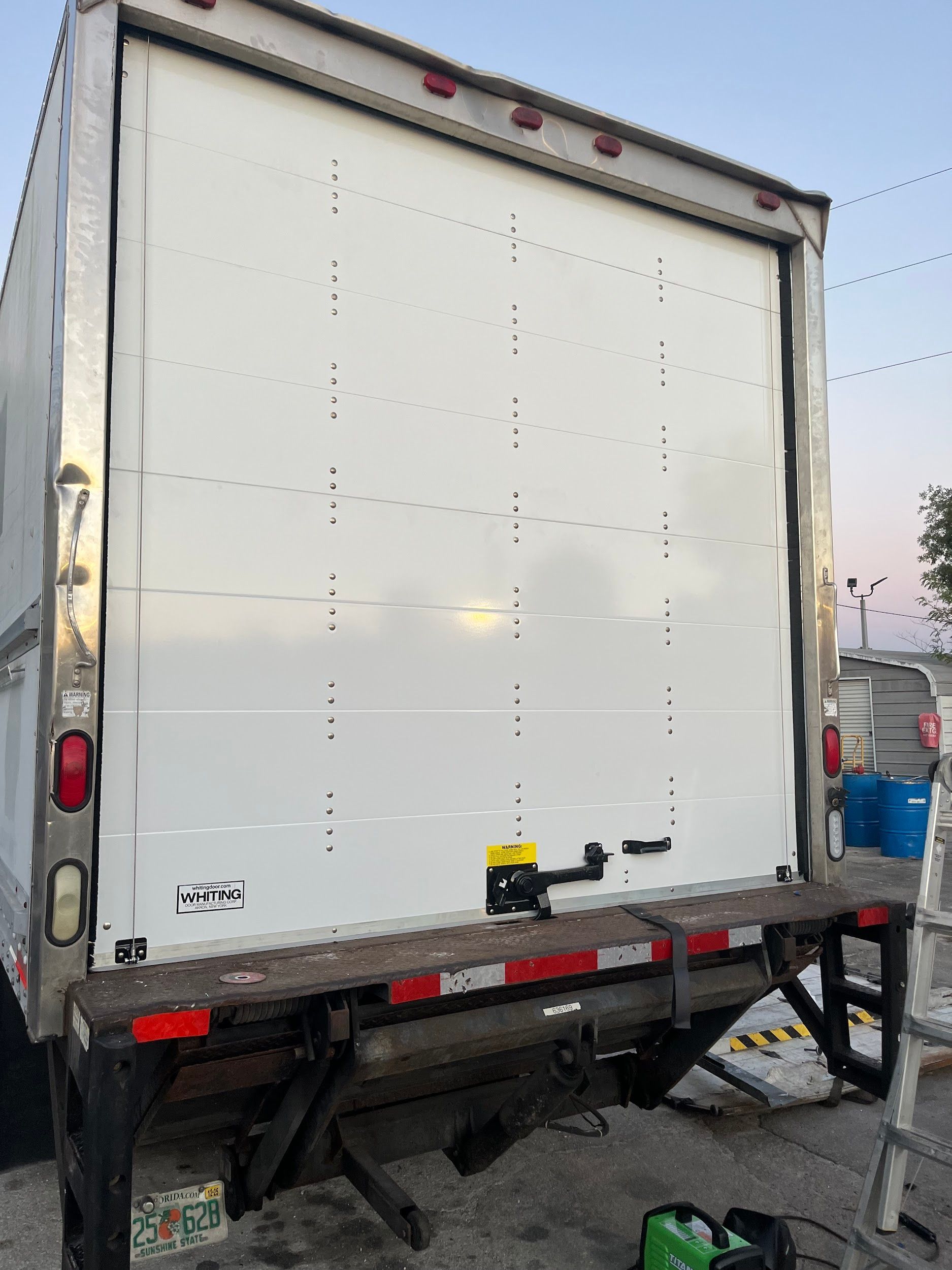 A white truck is parked in a parking lot with a ladder in front of it.