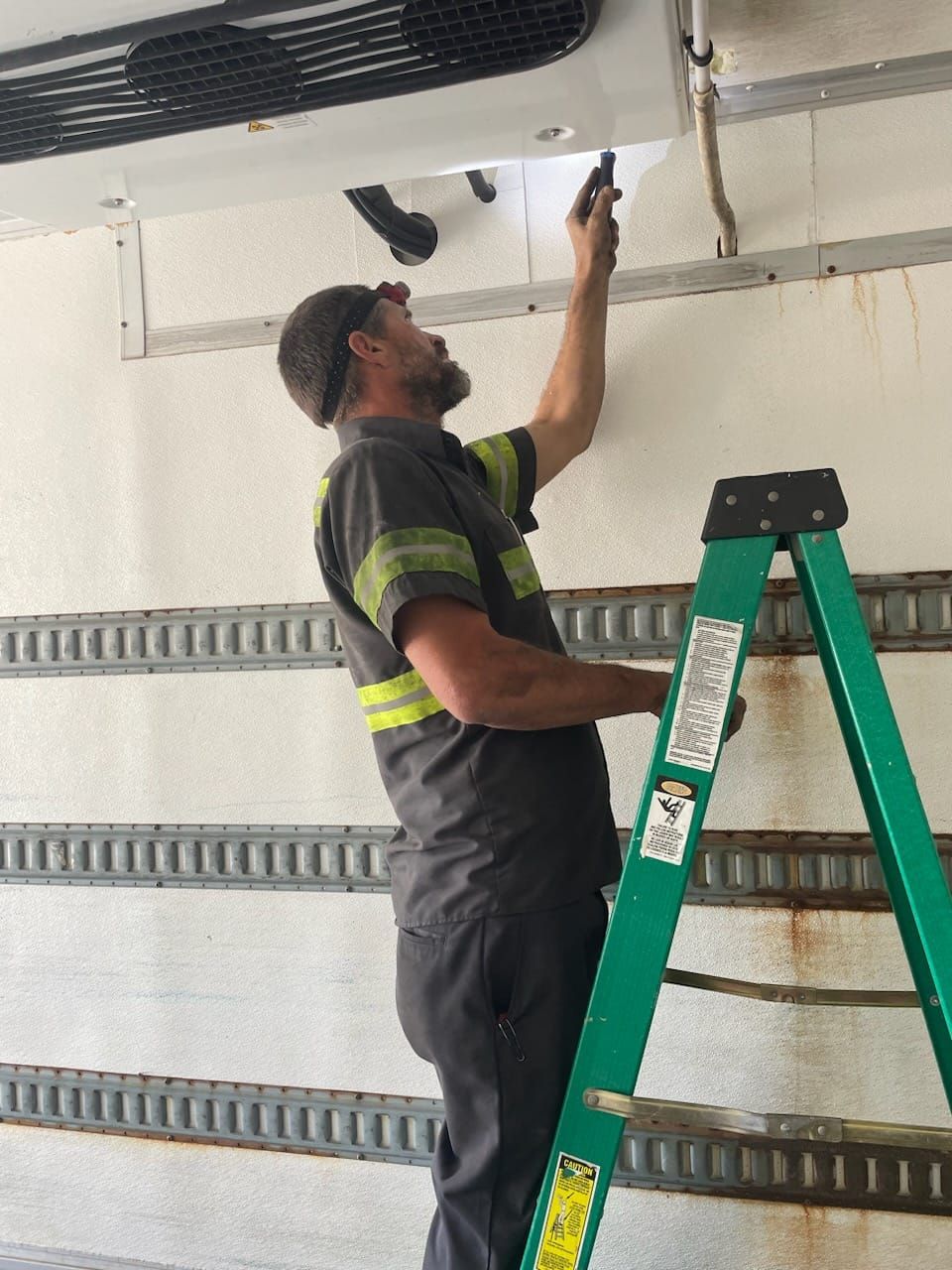 A man is standing on a ladder working on a refrigerator.