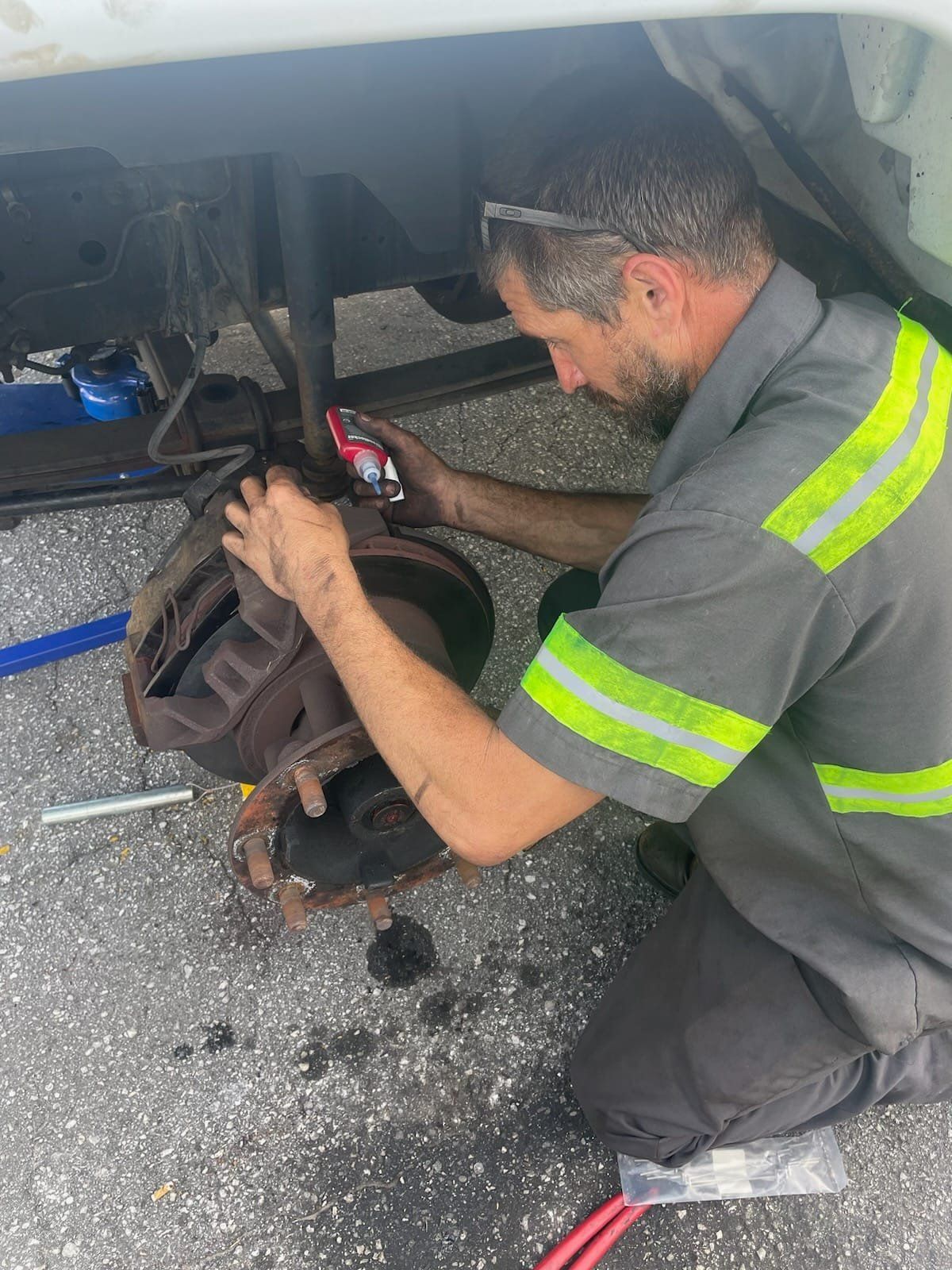 A man is kneeling down under a car and fixing a brake.