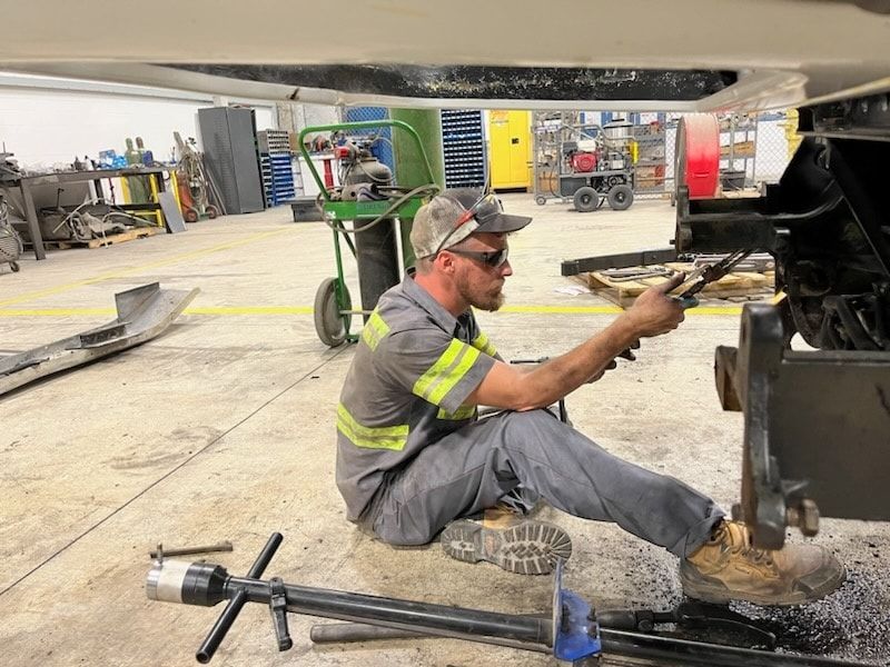 A man is sitting on the ground working on a vehicle in a garage.