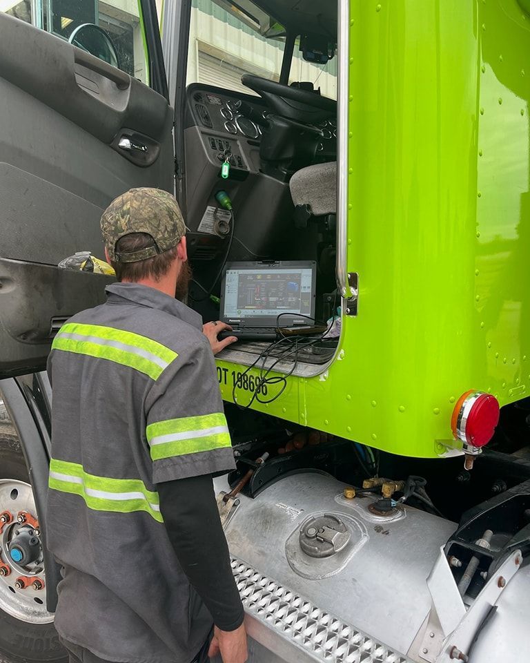A man is working on a green truck with a laptop.