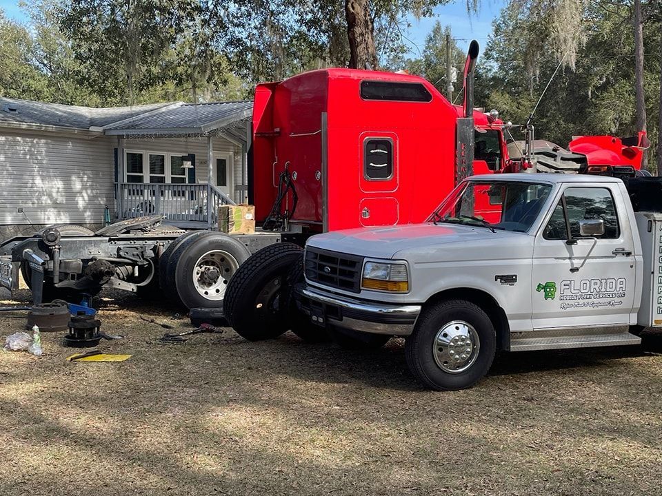A red semi truck and a white truck are parked in front of a house.