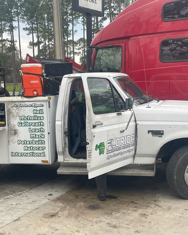A white truck with the door open is parked next to a red semi truck
