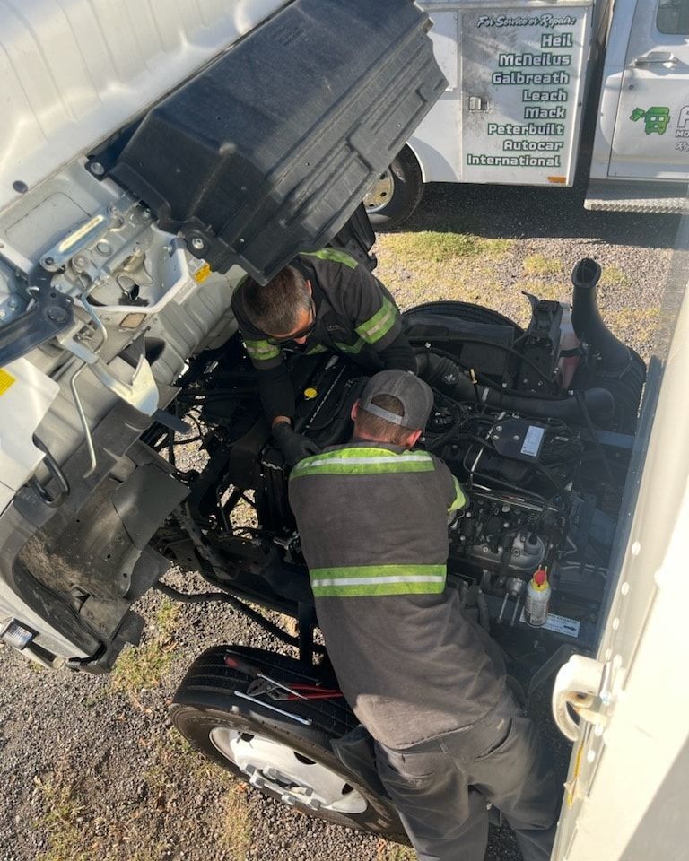 Two men are working on the engine of a truck.
