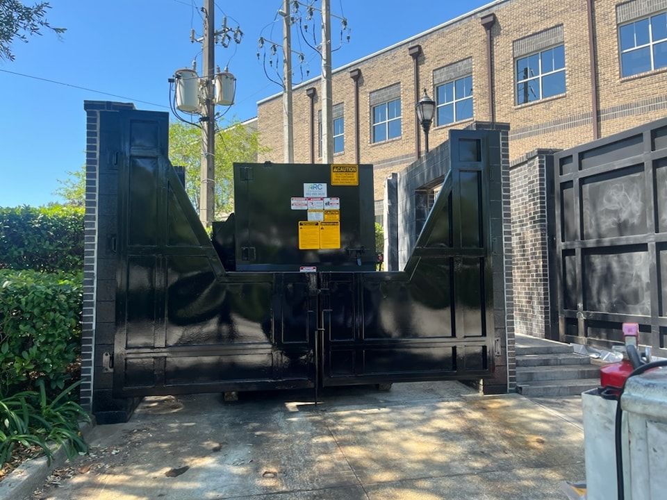 A large black dumpster is parked in front of a brick building.