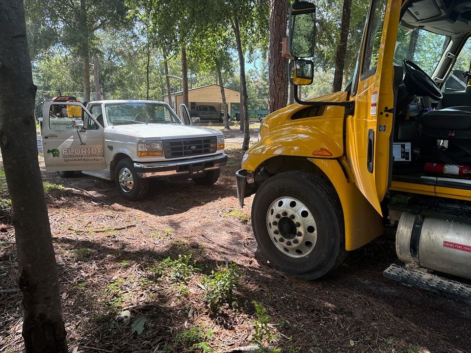 A yellow truck is parked next to a white truck in the woods.
