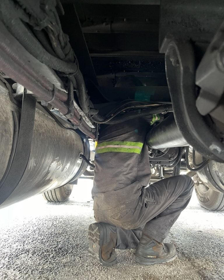 A man is kneeling under a truck and working on it.