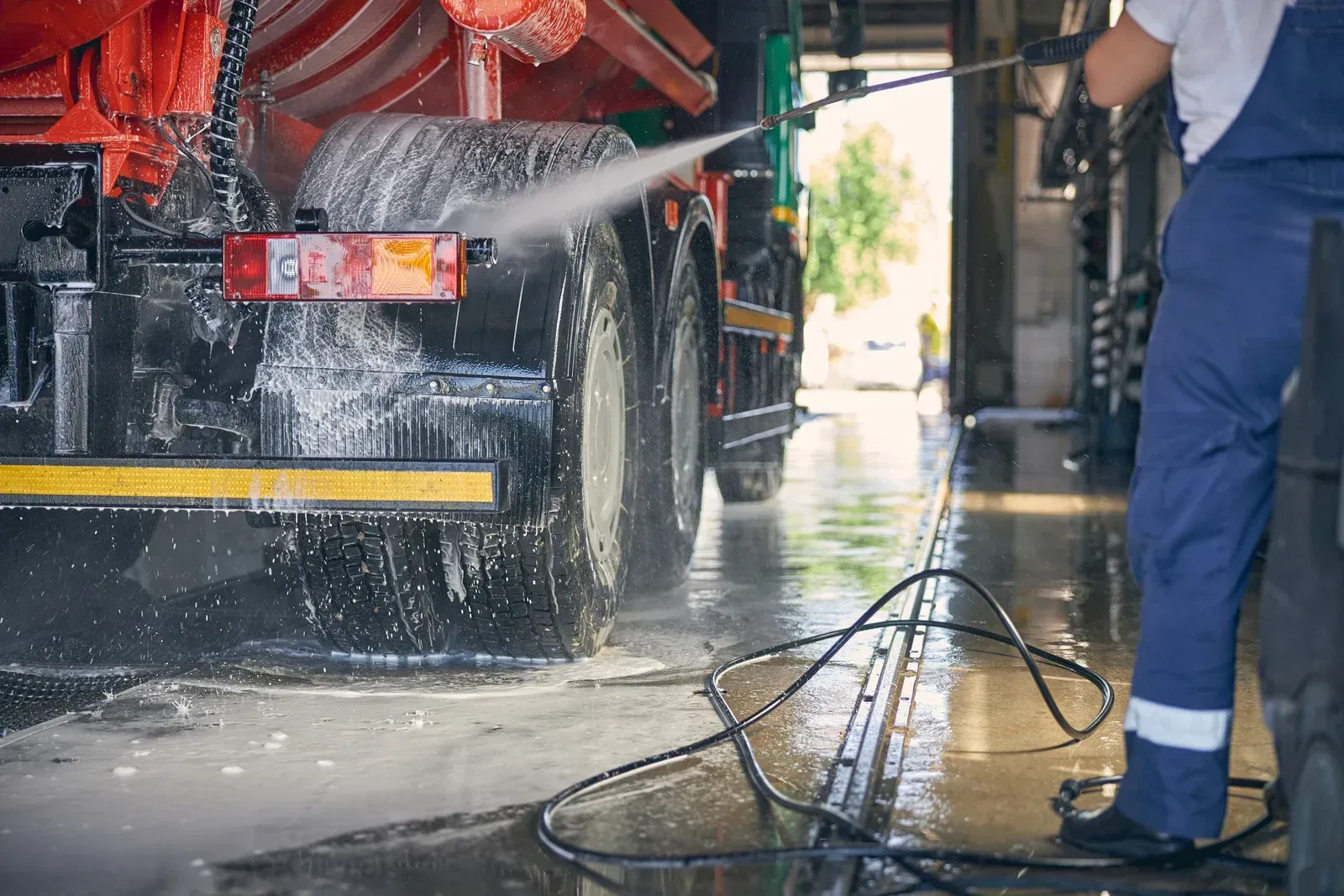 A man is washing a truck with a high pressure washer.